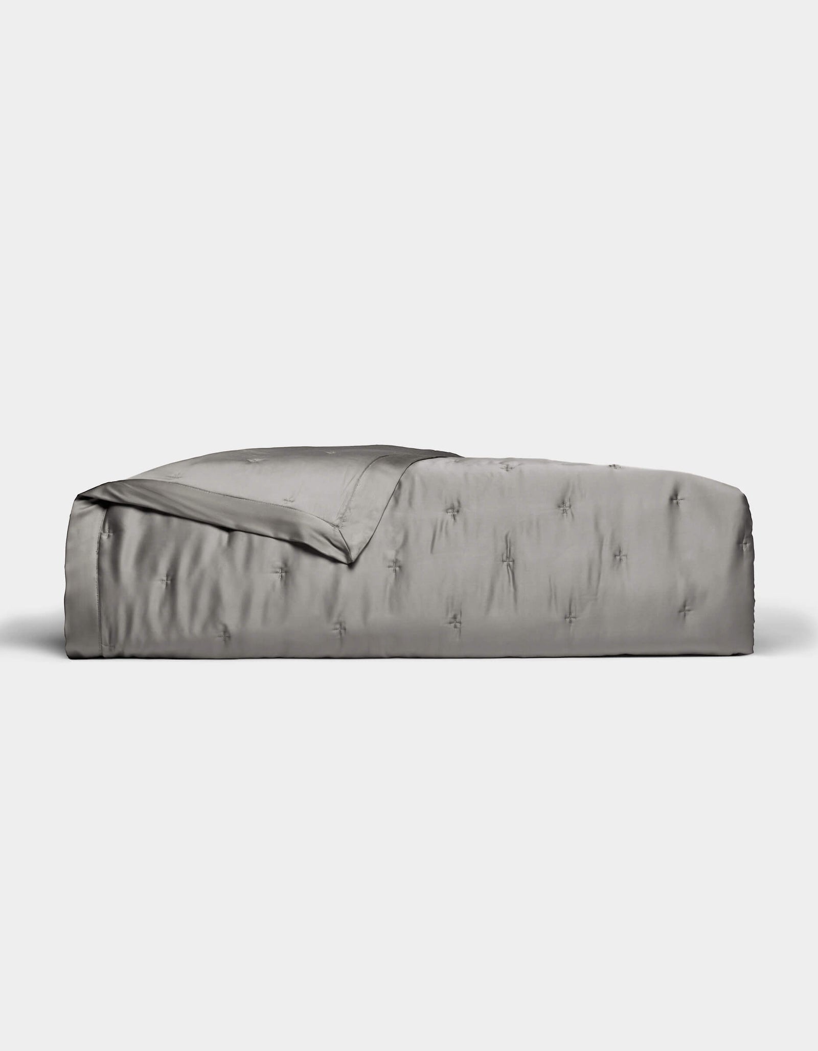 A neatly made bed features the Cozy Earth Bamboo Quilt in smooth, shiny silver-gray satin, partially folded back at the top, set against a plain white background.