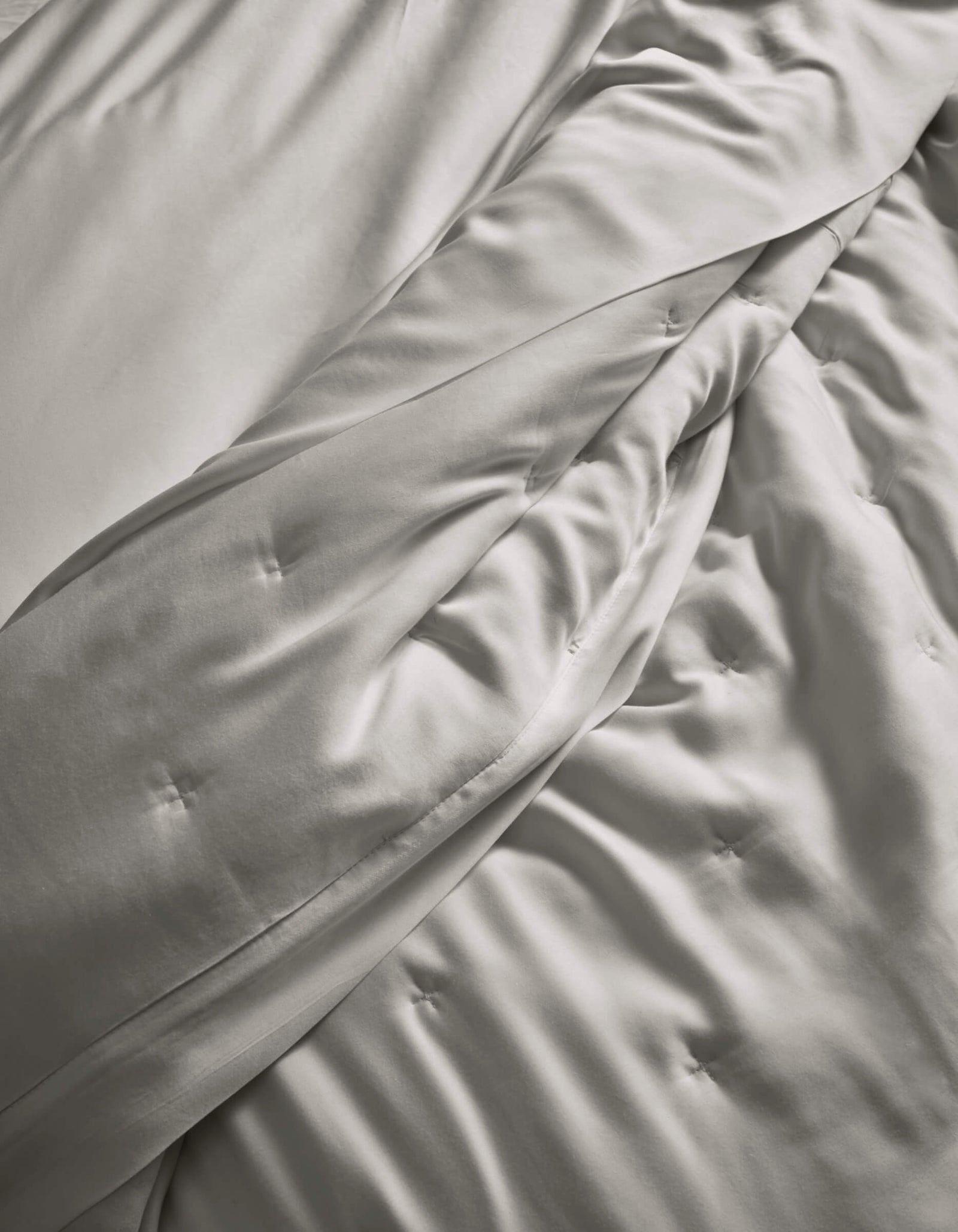 A close-up of the Cozy Earth Bamboo Quilt, in light gray, softly draped with subtle button tufting, highlights its smooth and silky fabric.