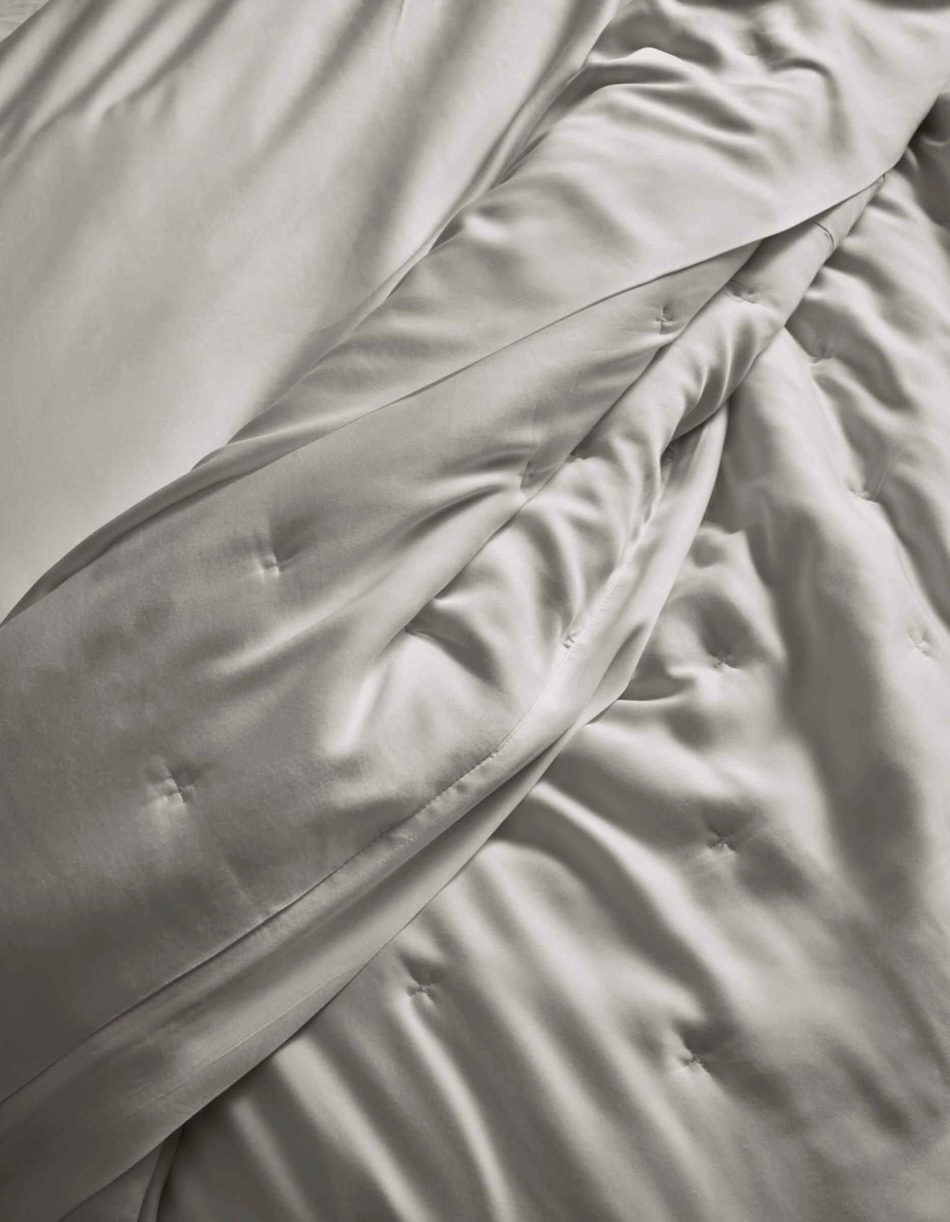 A close-up of the Cozy Earth Bamboo Quilt, in light gray, softly draped with subtle button tufting, highlights its smooth and silky fabric.