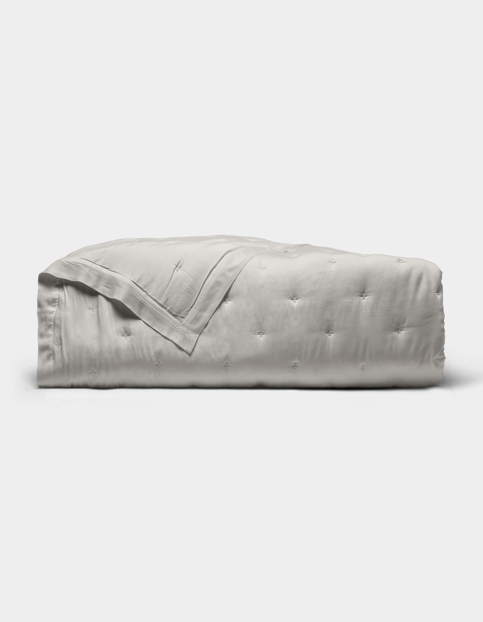 The Cozy Earth Bamboo Quilt, featuring a subtle tufted pattern and light gray color, is neatly folded against a plain white background.