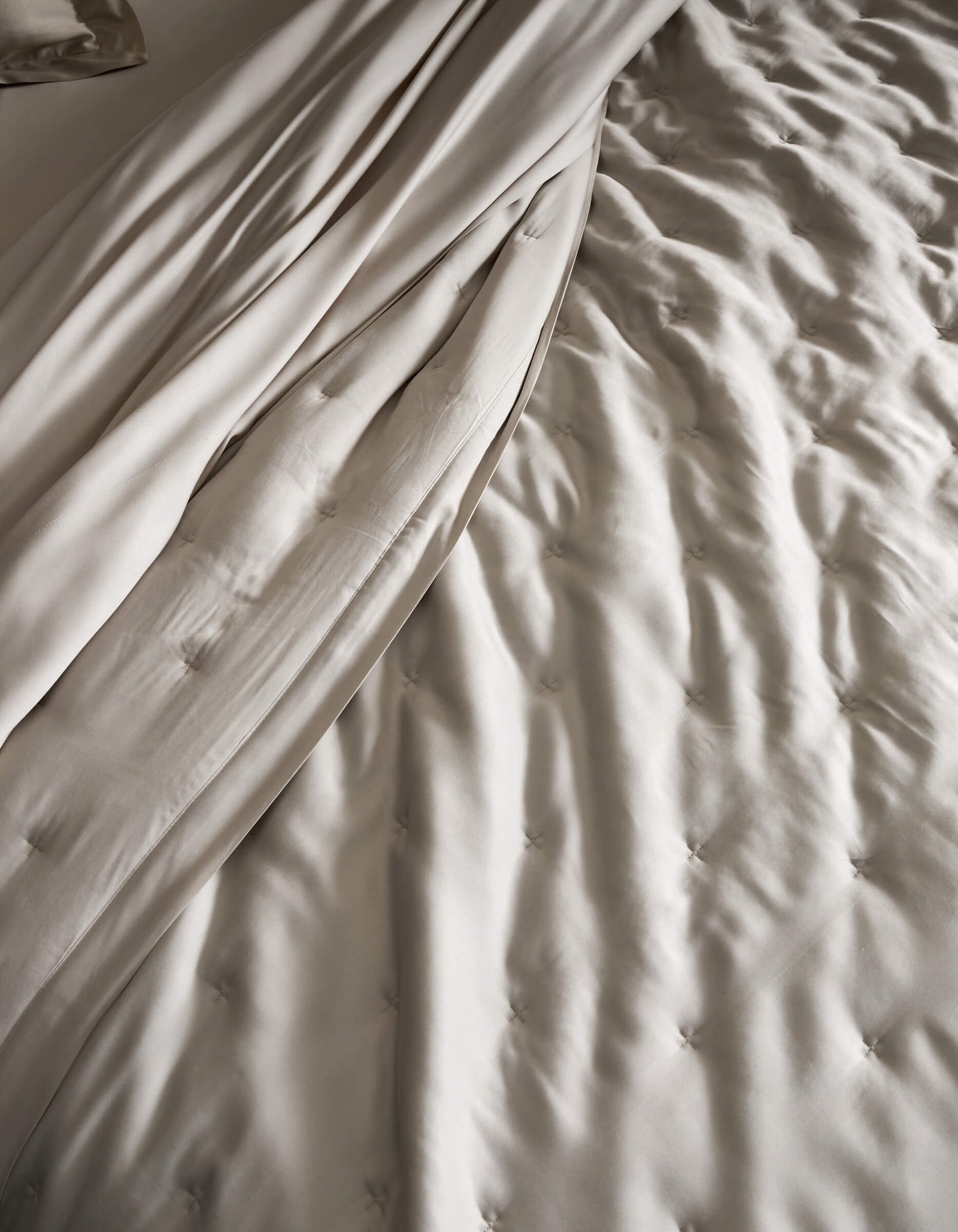 A close-up of a neatly made bed featuring the Cozy Earth Bamboo Quilt, showcasing its light beige, tufted design and smooth, draped sheets for a soft and elegant texture.