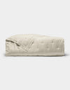 The Cozy Earth Bamboo Quilt, featuring a subtle quilted pattern and light beige color, is neatly folded and displayed against a plain white background.|Color:Oat