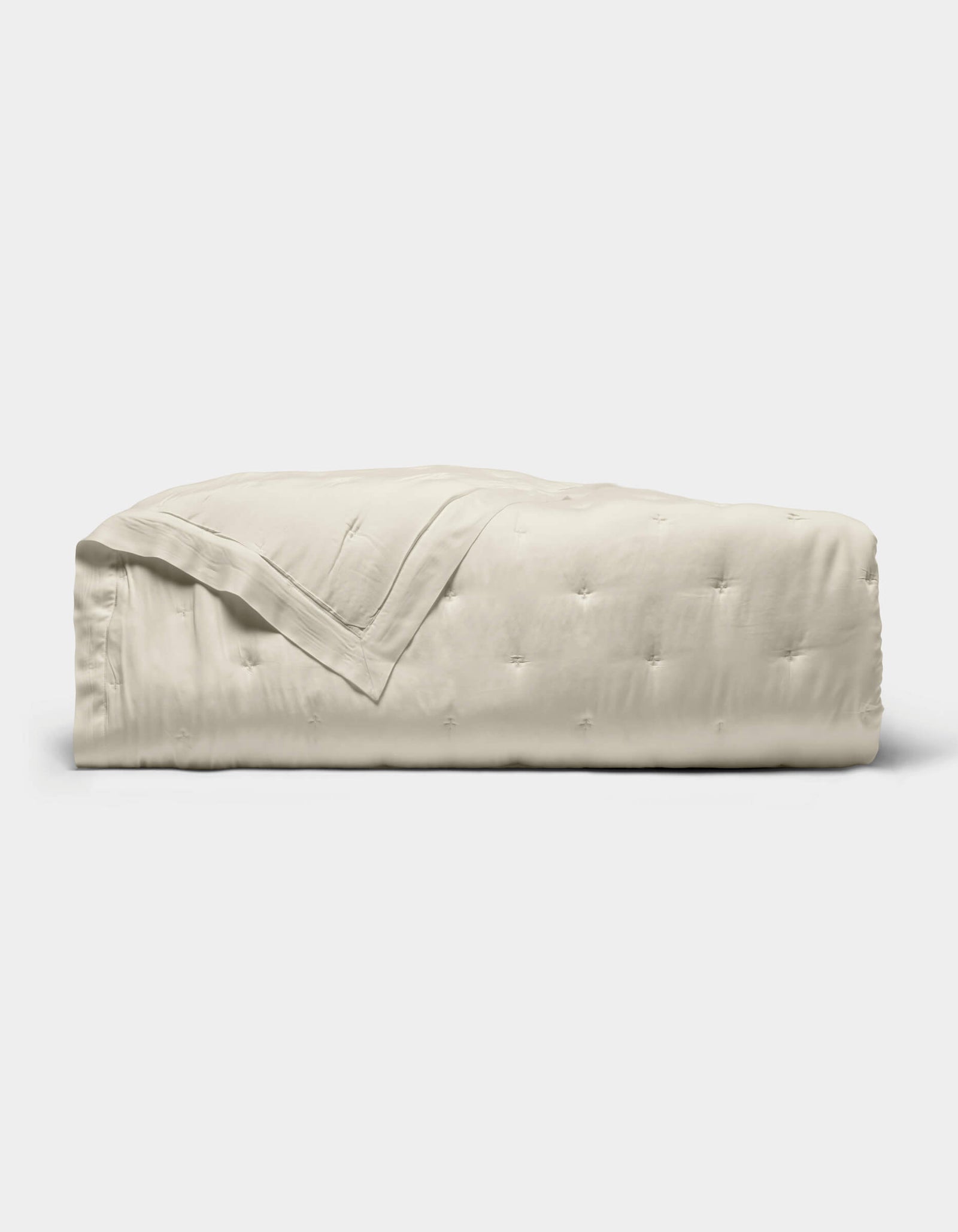 The Cozy Earth Bamboo Quilt, featuring a subtle quilted pattern and light beige color, is neatly folded and displayed against a plain white background.