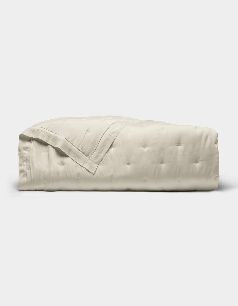 The Cozy Earth Bamboo Quilt, featuring a subtle quilted pattern and light beige color, is neatly folded and displayed against a plain white background.