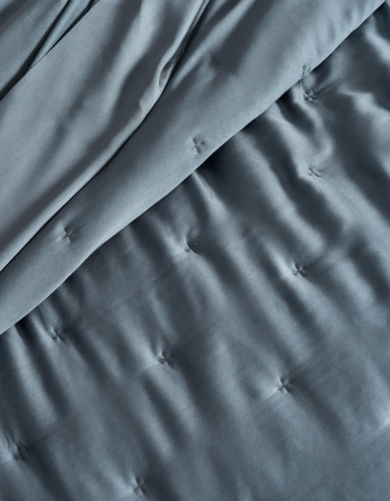 A close-up of the Cozy Earth Bamboo Quilt shows its dark gray, silky, and slightly shiny fabric with a quilted pattern, stitched tufts, and gentle folds.