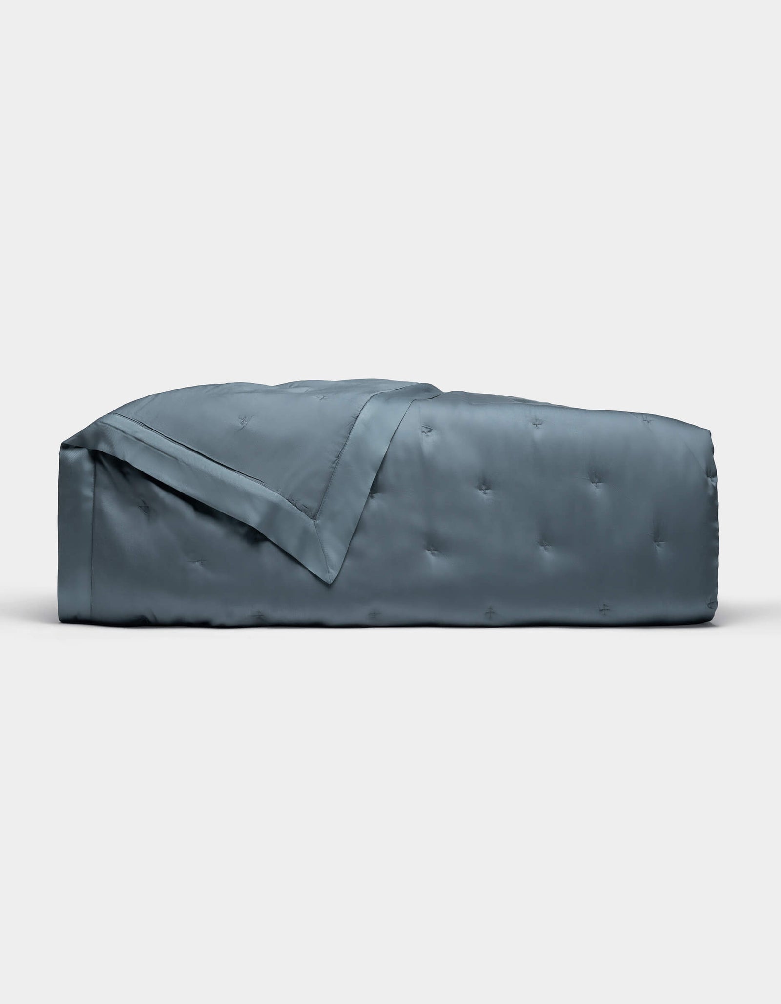 The Cozy Earth Bamboo Quilt, shown folded against a plain white background, features a blue-gray color with a subtle quilted pattern and smooth, shiny finish.