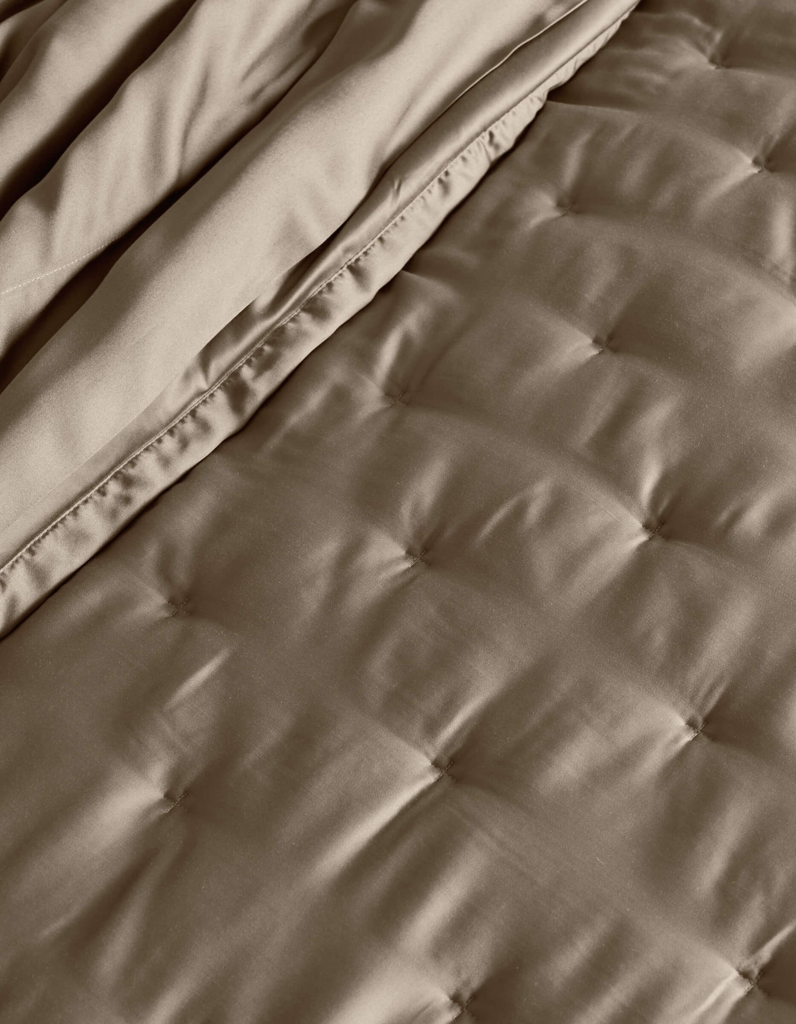 A close-up of the Cozy Earth Bamboo Quilt shows its quilted, taupe surface with stitched square patterns and a folded edge, highlighting the soft, smooth fabric texture.