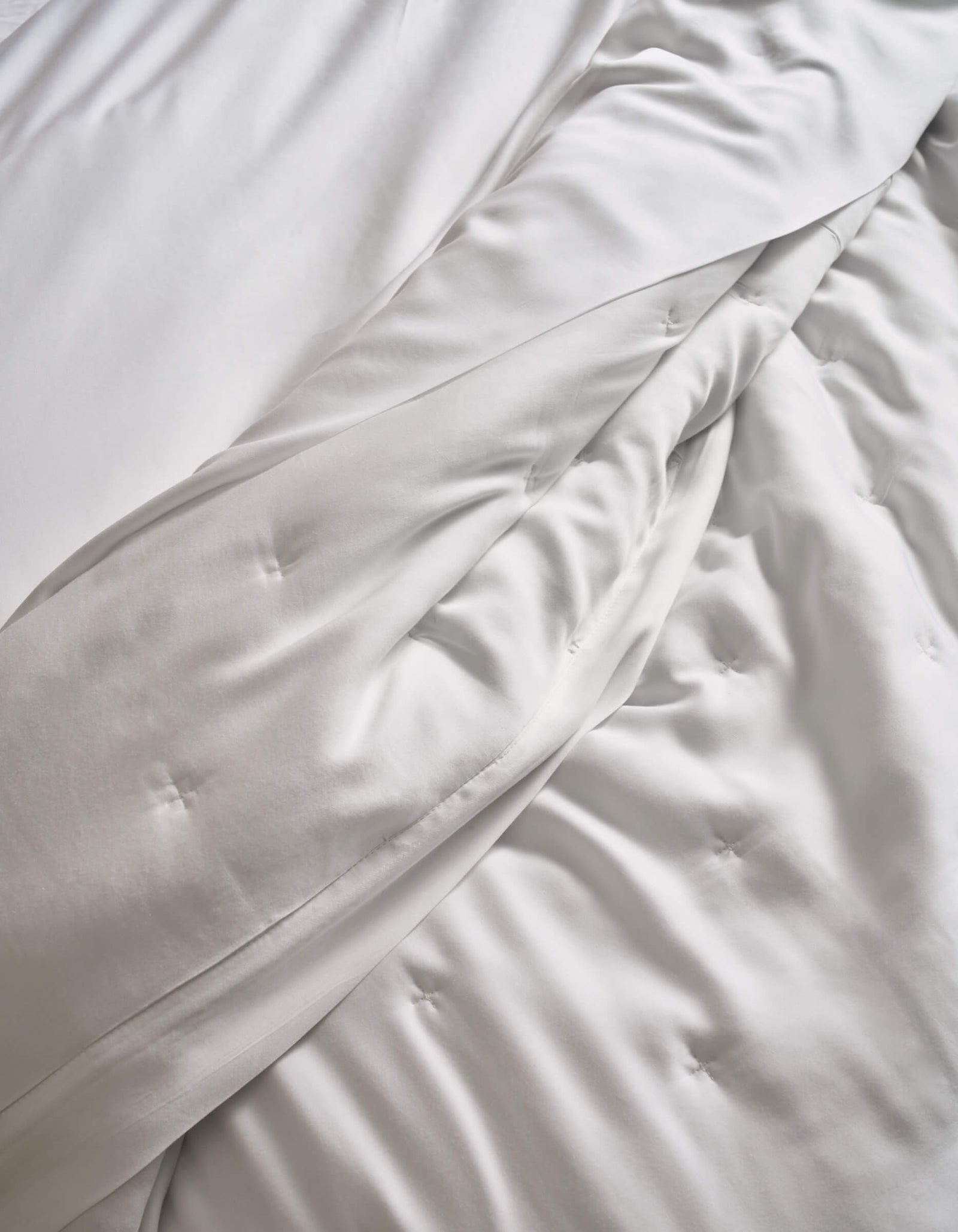 Close-up of a neatly made bed featuring Cozy Earth’s Bamboo Quilt, with soft, white, slightly wrinkled sheets and the plush, quilted comforter creating a cozy and inviting look.