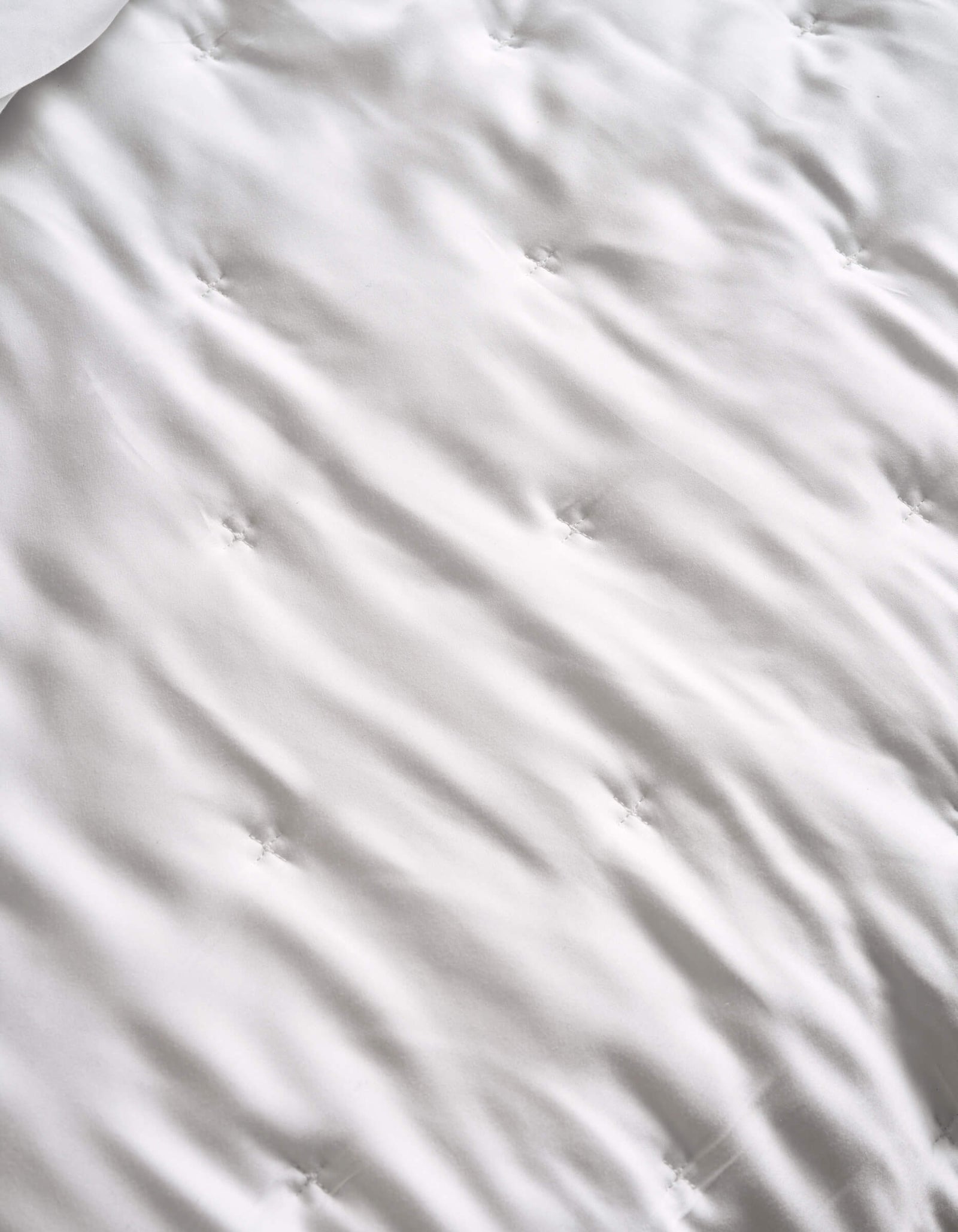A close-up of the Cozy Earth Bamboo Quilt’s white, tufted surface features gentle waves and sewn dimples, hinting at its soft, quilted texture.