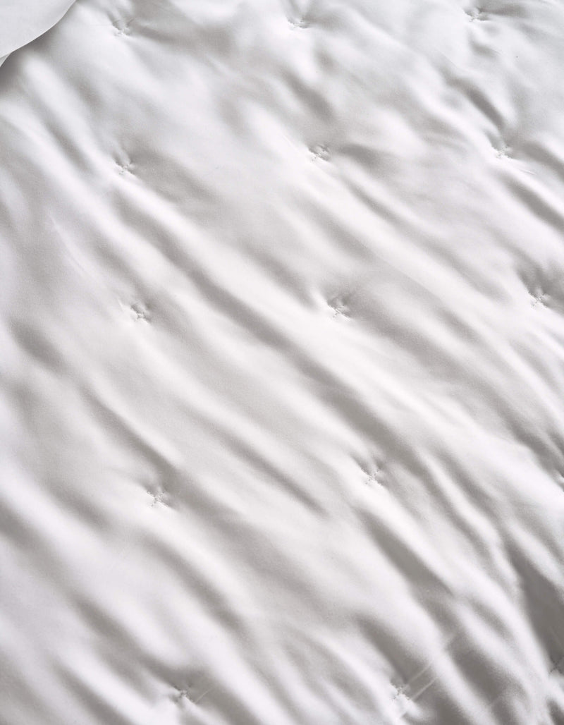 A close-up of the Cozy Earth Bamboo Quilt’s white, tufted surface features gentle waves and sewn dimples, hinting at its soft, quilted texture.