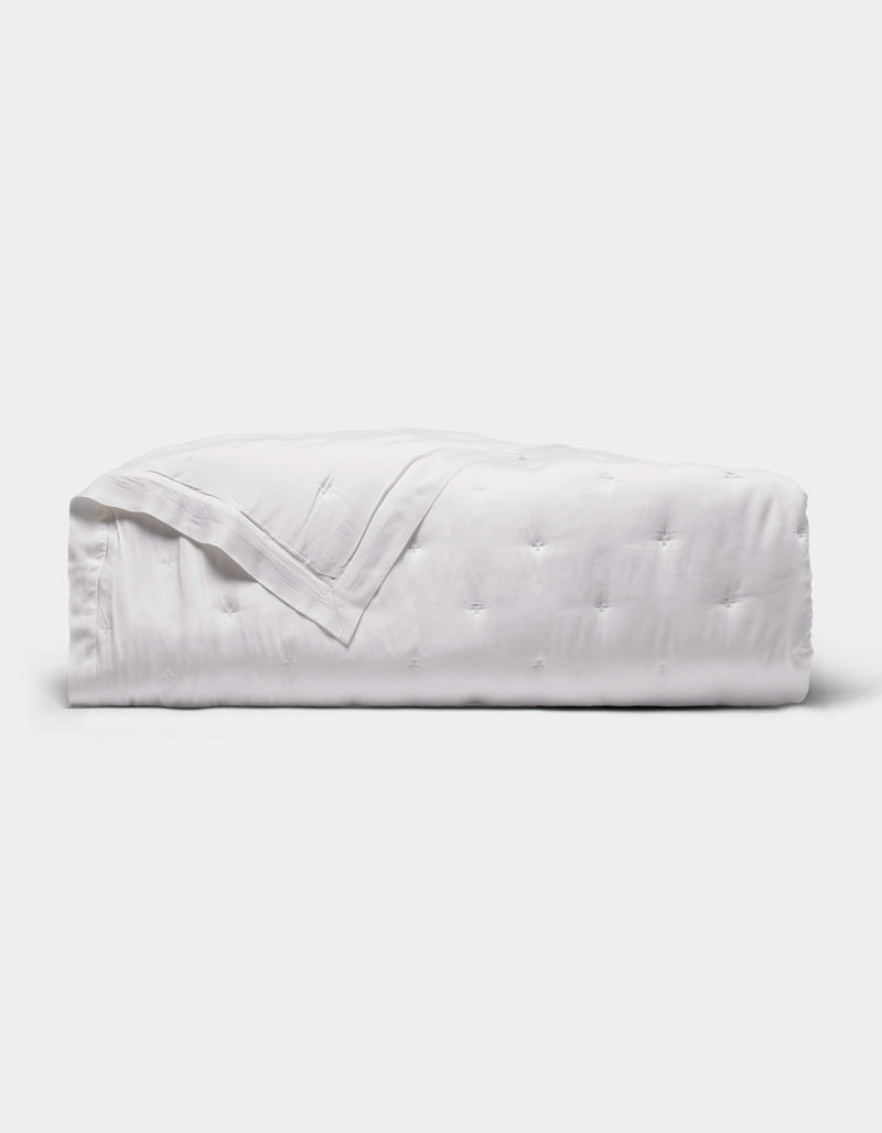 The Cozy Earth Bamboo Quilt is a neatly folded white quilt with a subtle quilted pattern, displayed against a plain light gray background.