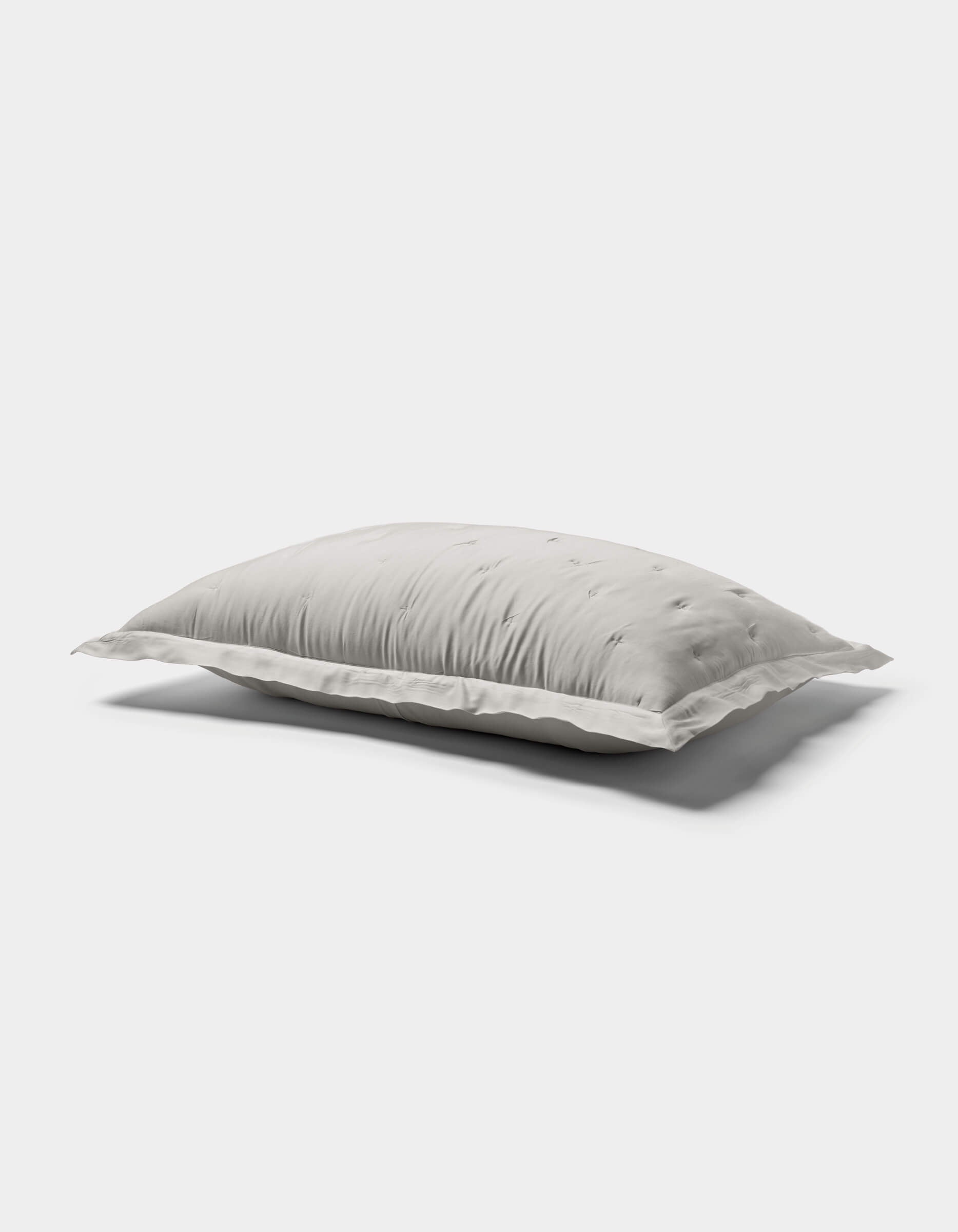 A white, rectangular Bamboo Quilted Sham by Cozy Earth with a soft, fluffy texture rests on a plain light gray background, casting a gentle shadow beneath it.|Color:Light Grey