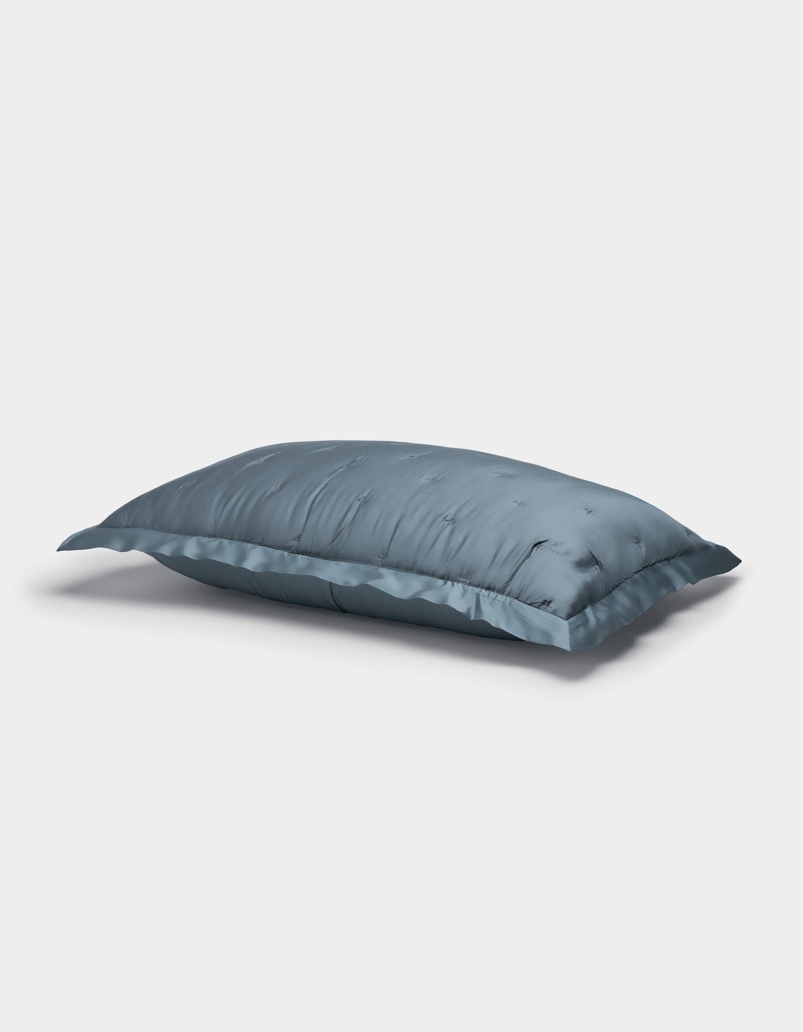 A blue Bamboo Quilted Sham by Cozy Earth lies on a white background, showcasing its soft, slightly wrinkled surface and smooth, glossy fabric.