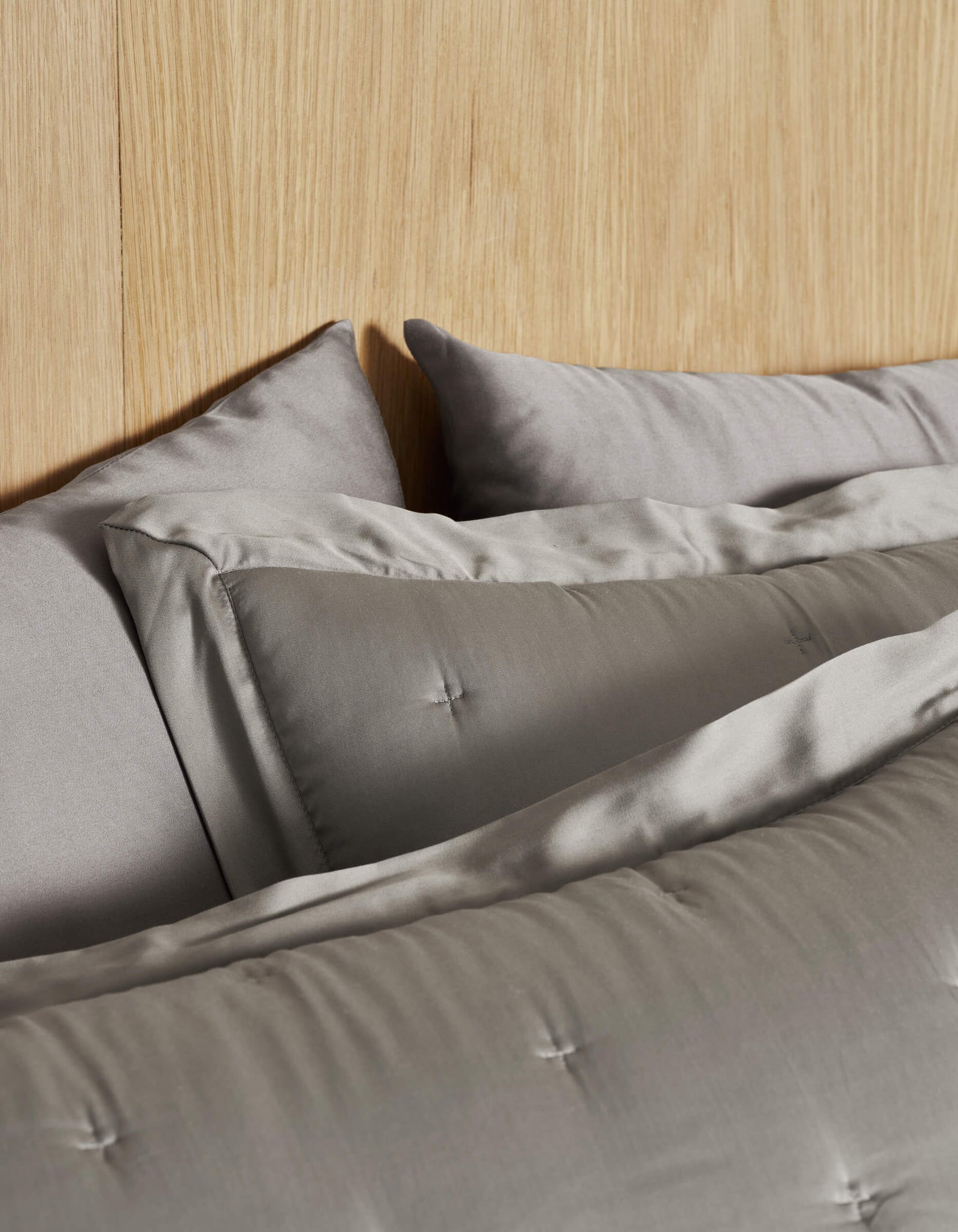 A bed featuring Cozy Earth's Bamboo Quilted Shams in light gray and a matching comforter with stitched detailing. A light wood headboard adds warmth to the neutral bedding ensemble.