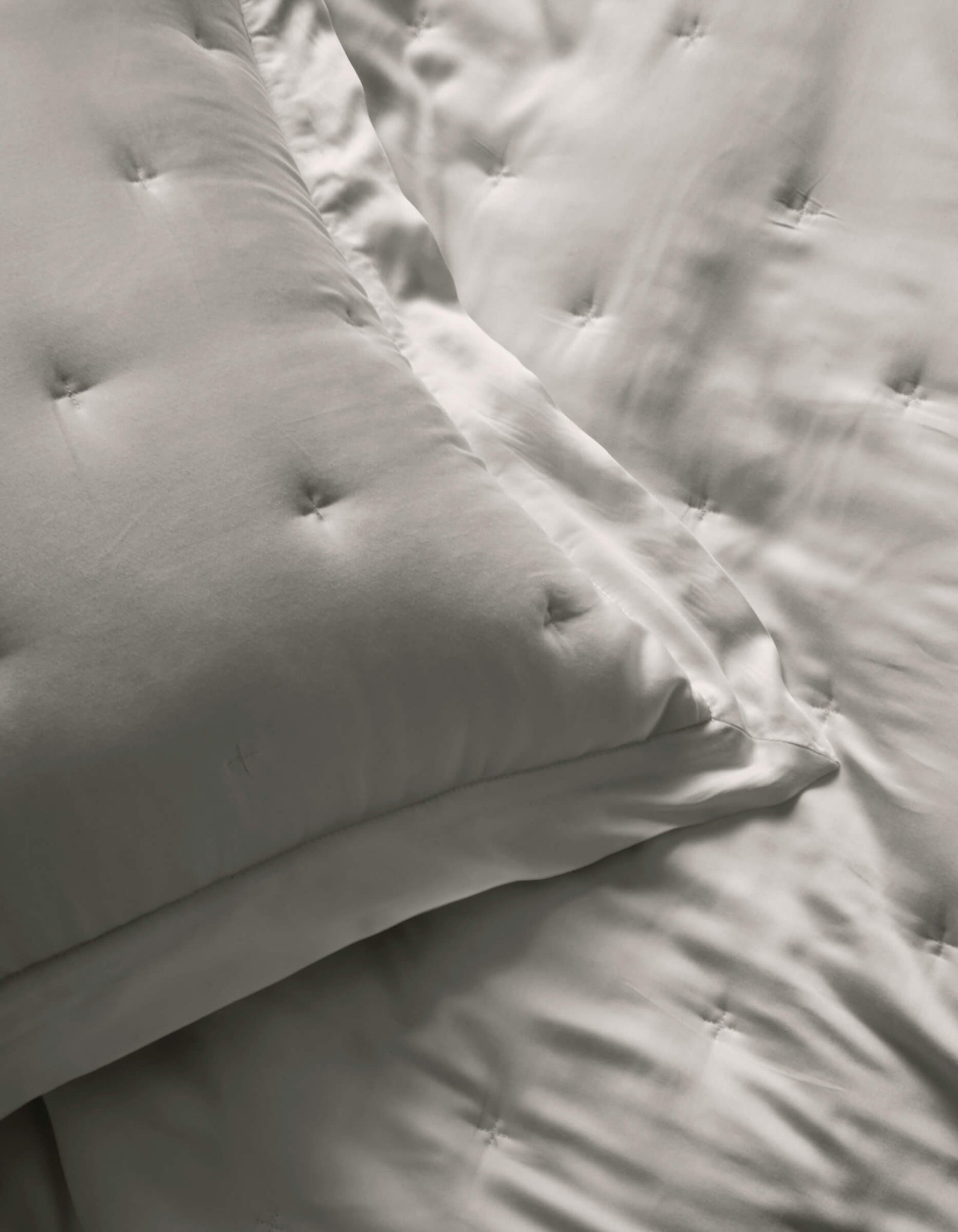 Close-up of two Cozy Earth Bamboo Quilted Shams and a matching comforter, all in smooth, light gray satin fabric with a subtle sheen.