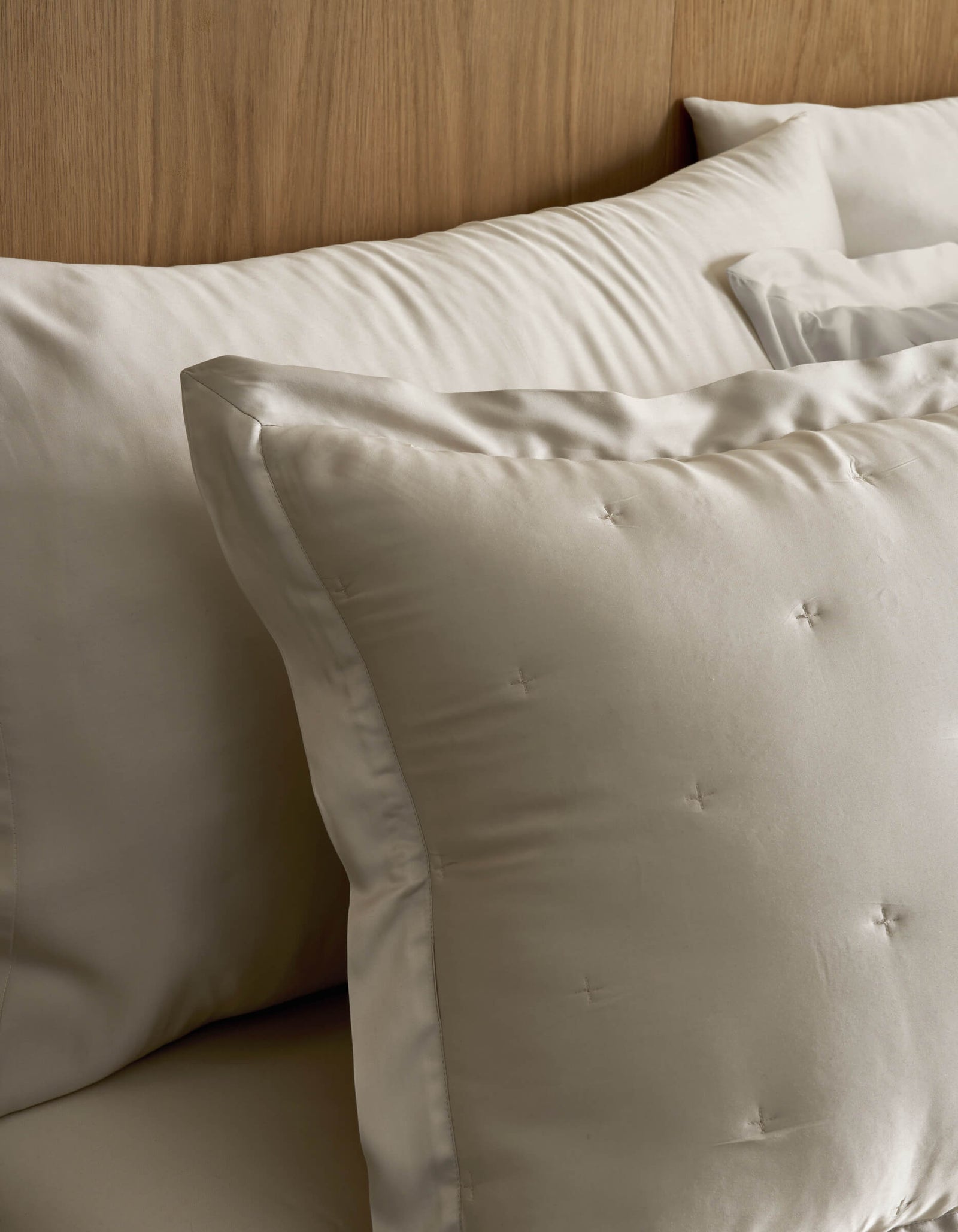 Close-up of Cozy Earth Bamboo Quilted Shams on a bed, featuring cream-colored square shams with subtle tufted details and larger rectangular pillows arranged neatly against a wooden headboard.
