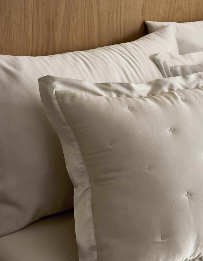 Close-up of Cozy Earth Bamboo Quilted Shams on a bed, featuring cream-colored square shams with subtle tufted details and larger rectangular pillows arranged neatly against a wooden headboard.