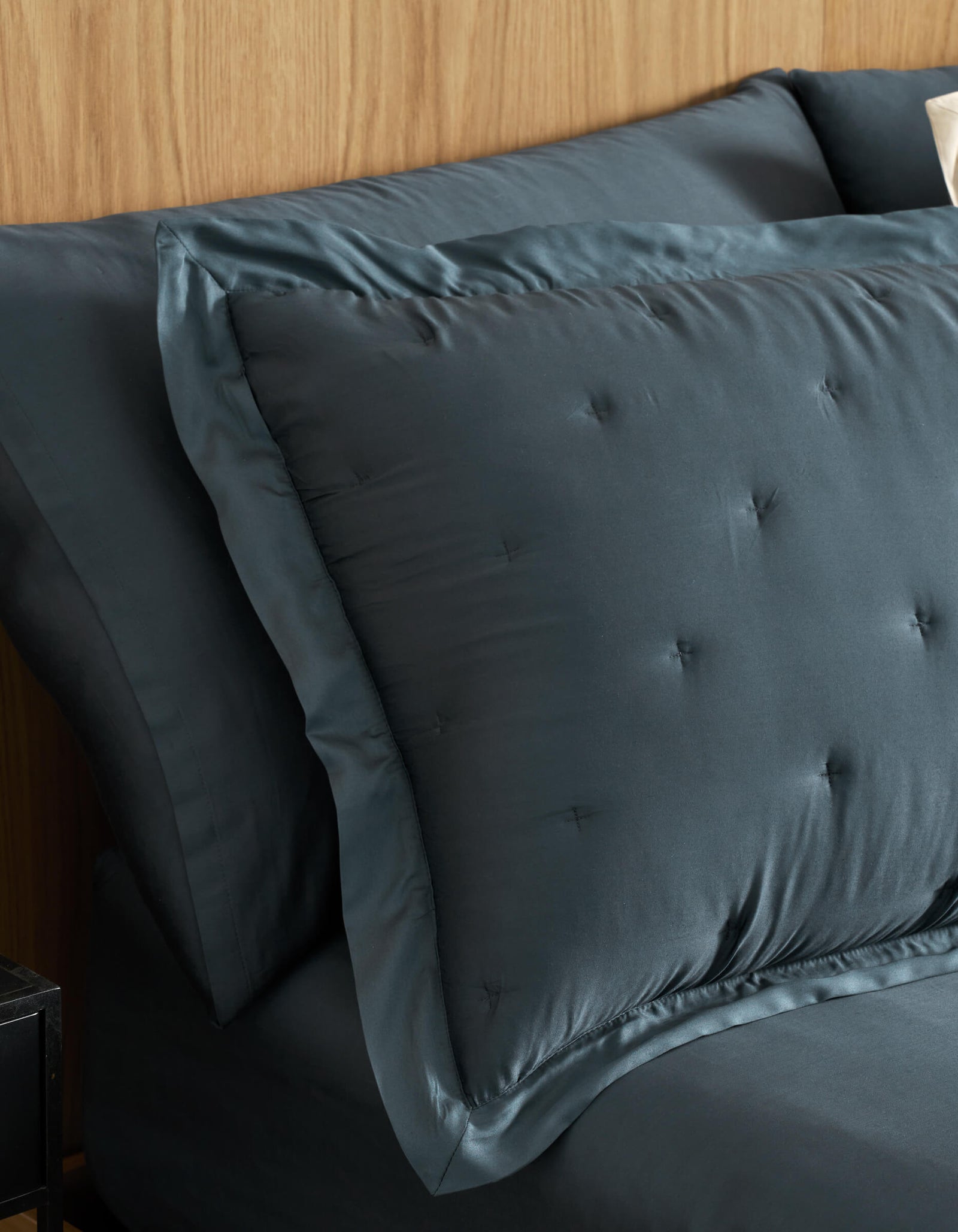 A close-up of a neatly made bed features Cozy Earth Bamboo Quilted Shams and matching sheets in dark blue, set against a light wood headboard.