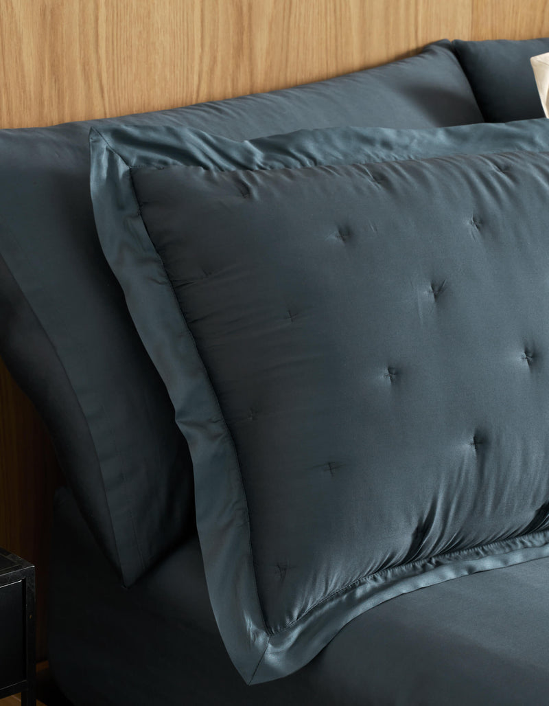 A close-up of a neatly made bed features Cozy Earth Bamboo Quilted Shams and matching sheets in dark blue, set against a light wood headboard.