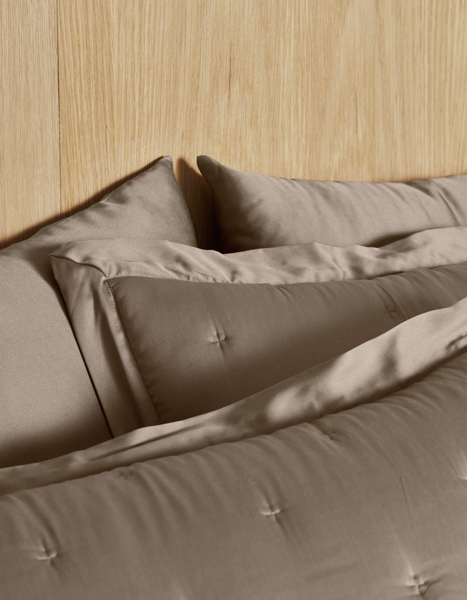 Close-up of Cozy Earth Bamboo Quilted Shams, neatly arranged in taupe on a bed with a light wood headboard, creating a calm and cozy atmosphere.
