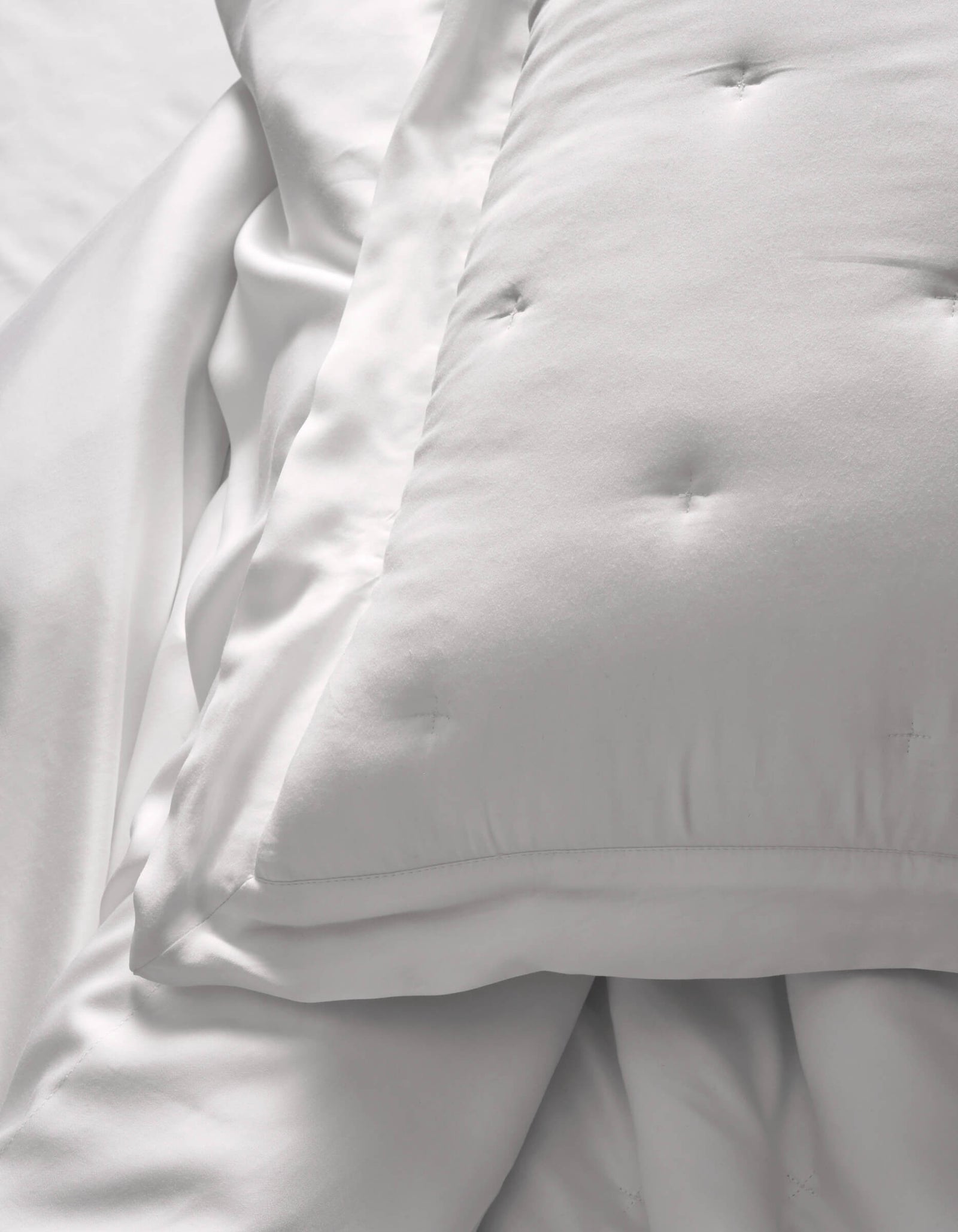 A close-up of Cozy Earth Bamboo Quilted Shams resting on smooth white sheets creates a soft, clean look. The bedding appears fluffy and inviting.