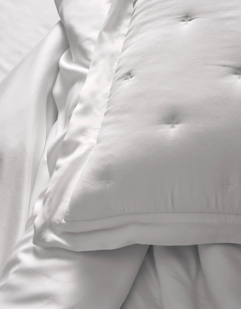 A close-up of Cozy Earth Bamboo Quilted Shams resting on smooth white sheets creates a soft, clean look. The bedding appears fluffy and inviting.