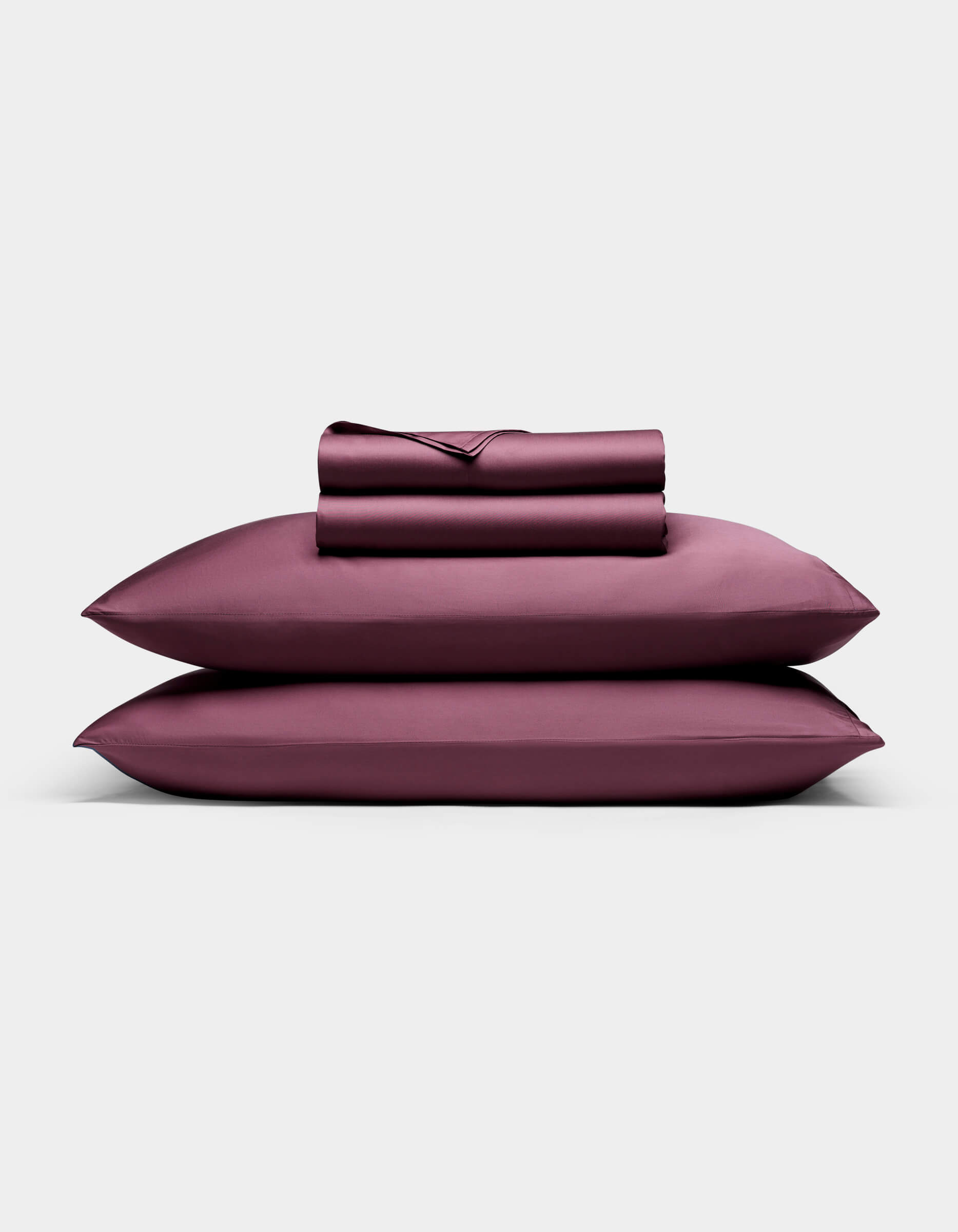 The Cozy Earth Bamboo Sheet Set in deep plum features two pillowcases stacked horizontally with a fitted and flat sheet folded on top, all arranged neatly against a plain light background.|Color:Mulberry