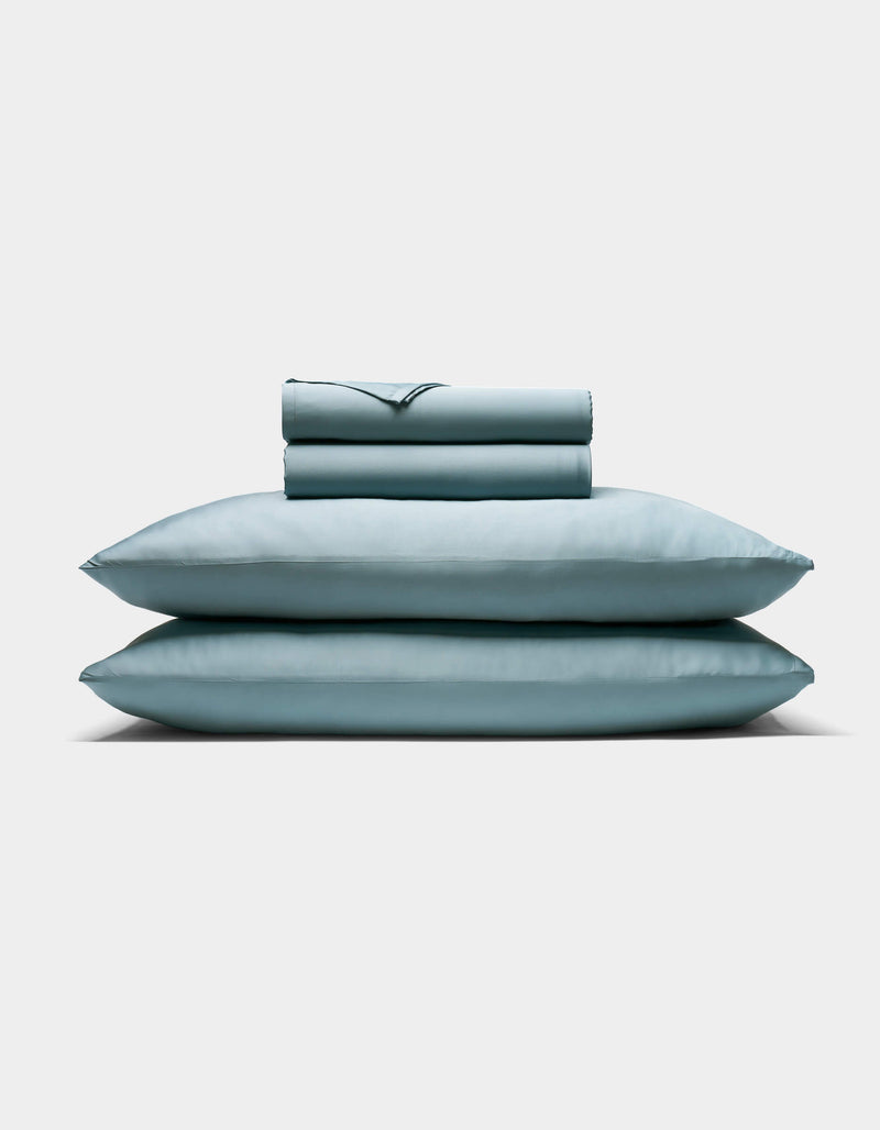 The Cozy Earth Bamboo Sheet Set, featuring two pillows and a folded sheet in pale blue, is neatly stacked against a plain white background.