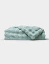 The Bubble Cuddle Blanket by Cozy Earth, in a soft light blue, is shown folded neatly on a white background.|Color:Tide
