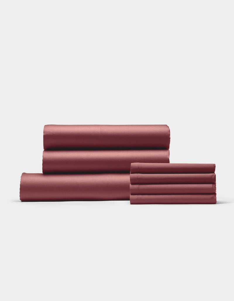 The Cozy Earth Bamboo Bedding Core Bundle, featuring four folded reddish-brown bed sheets and two matching pillowcases, is neatly stacked against a plain white background.
