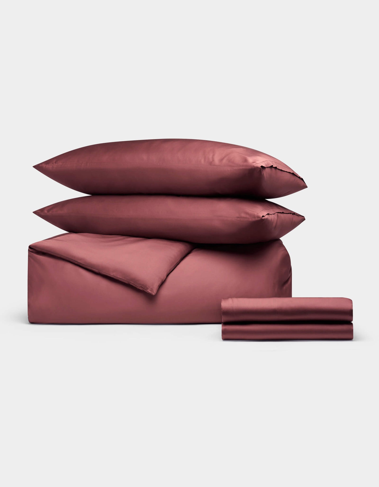 The Cozy Earth Bamboo Bedding Deluxe Bundle, in dusty rose, includes two pillows, a duvet, and sheets neatly folded and displayed on a plain white background.