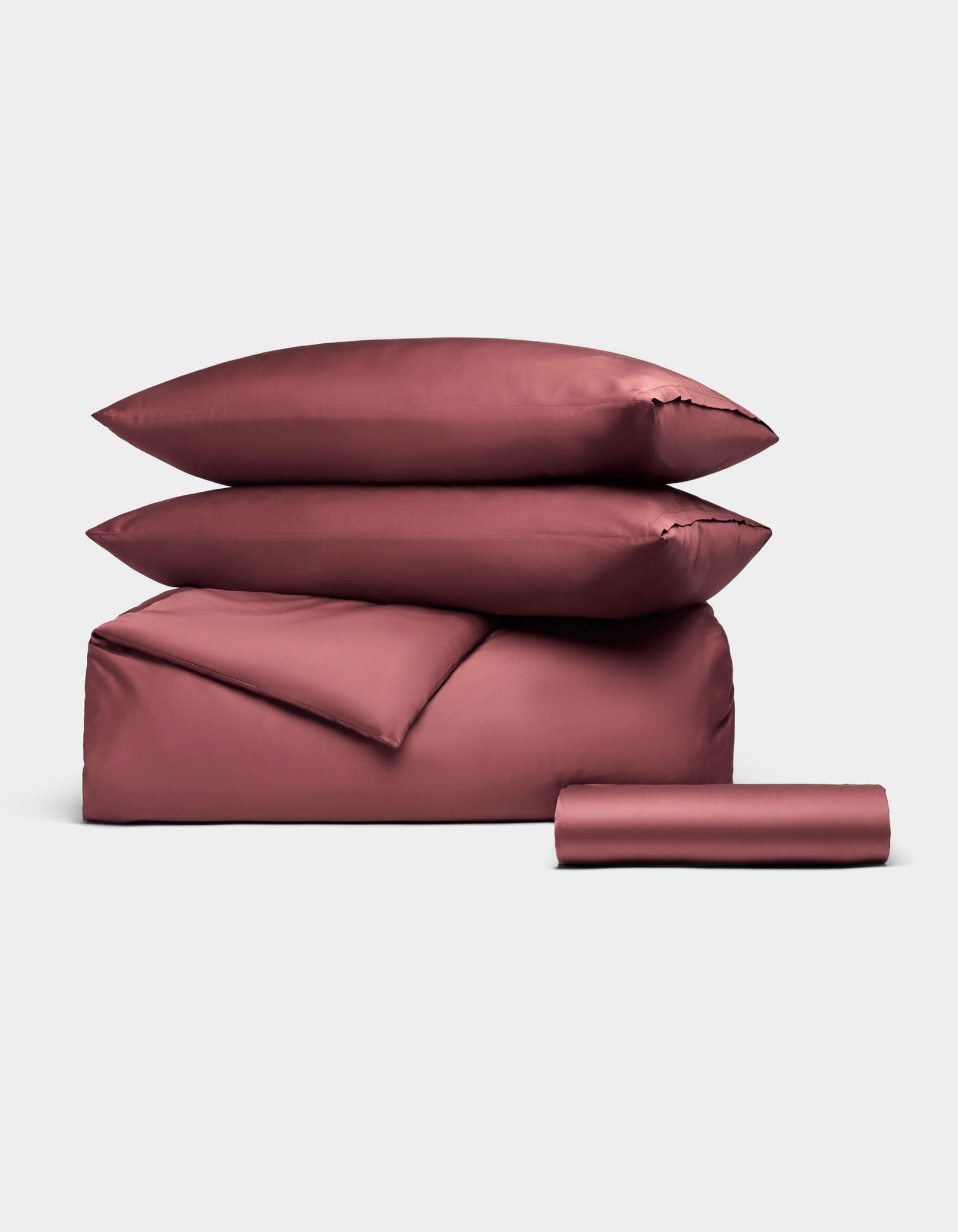 The Cozy Earth Bamboo Bedding Essential Bundle, featuring two stacked pillows, a duvet cover, and a folded sheet in mauve, is neatly displayed against a plain light background.