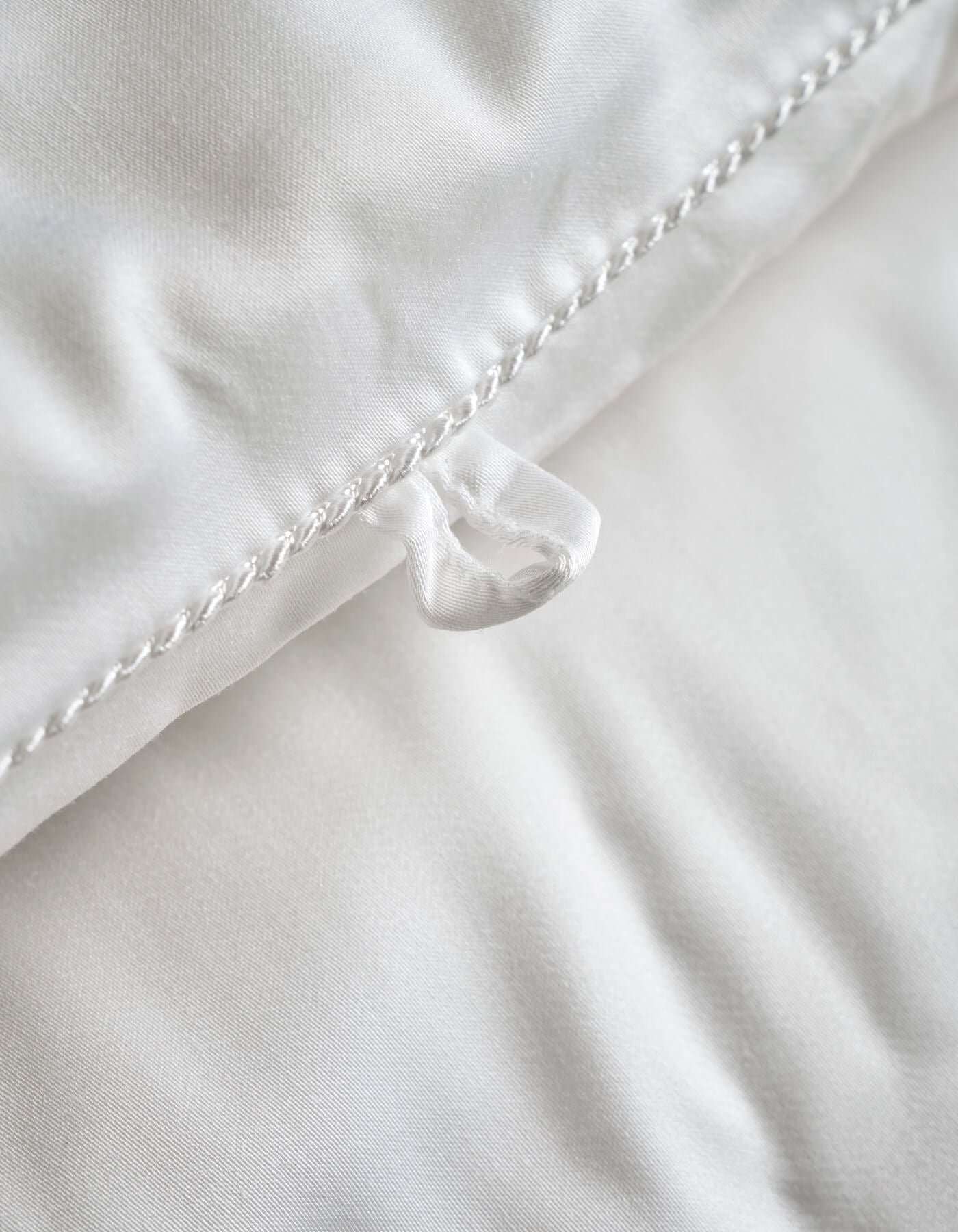 Close-up of the Cozy Earth Silk Comforter, featuring a white surface with a fabric loop sewn into the edge and detailed seam stitching. The smooth and soft texture showcases its luxurious comfort.