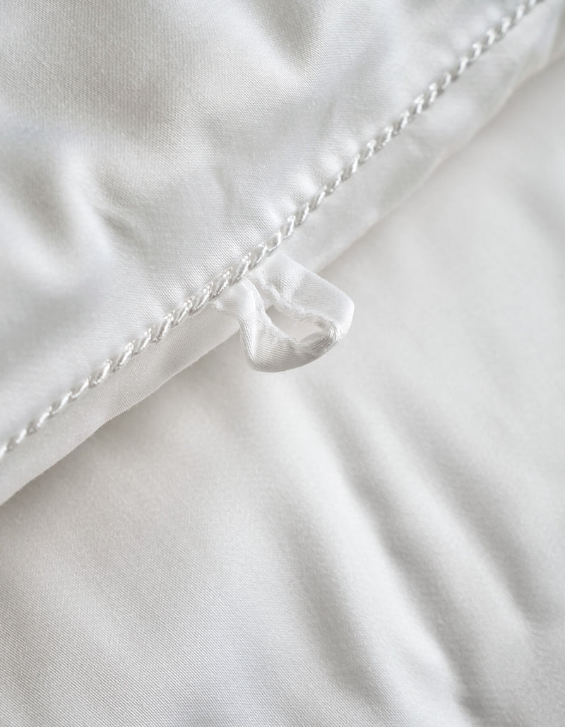 Close-up of the Cozy Earth Silk Comforter, featuring a white surface with a fabric loop sewn into the edge and detailed seam stitching. The smooth and soft texture showcases its luxurious comfort.