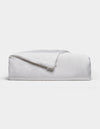 A neatly folded, fluffy Silk Comforter by Cozy Earth is placed against a plain light background. The fabric appears smooth and soft, highlighting its plush and inviting texture.|Filling:Extra