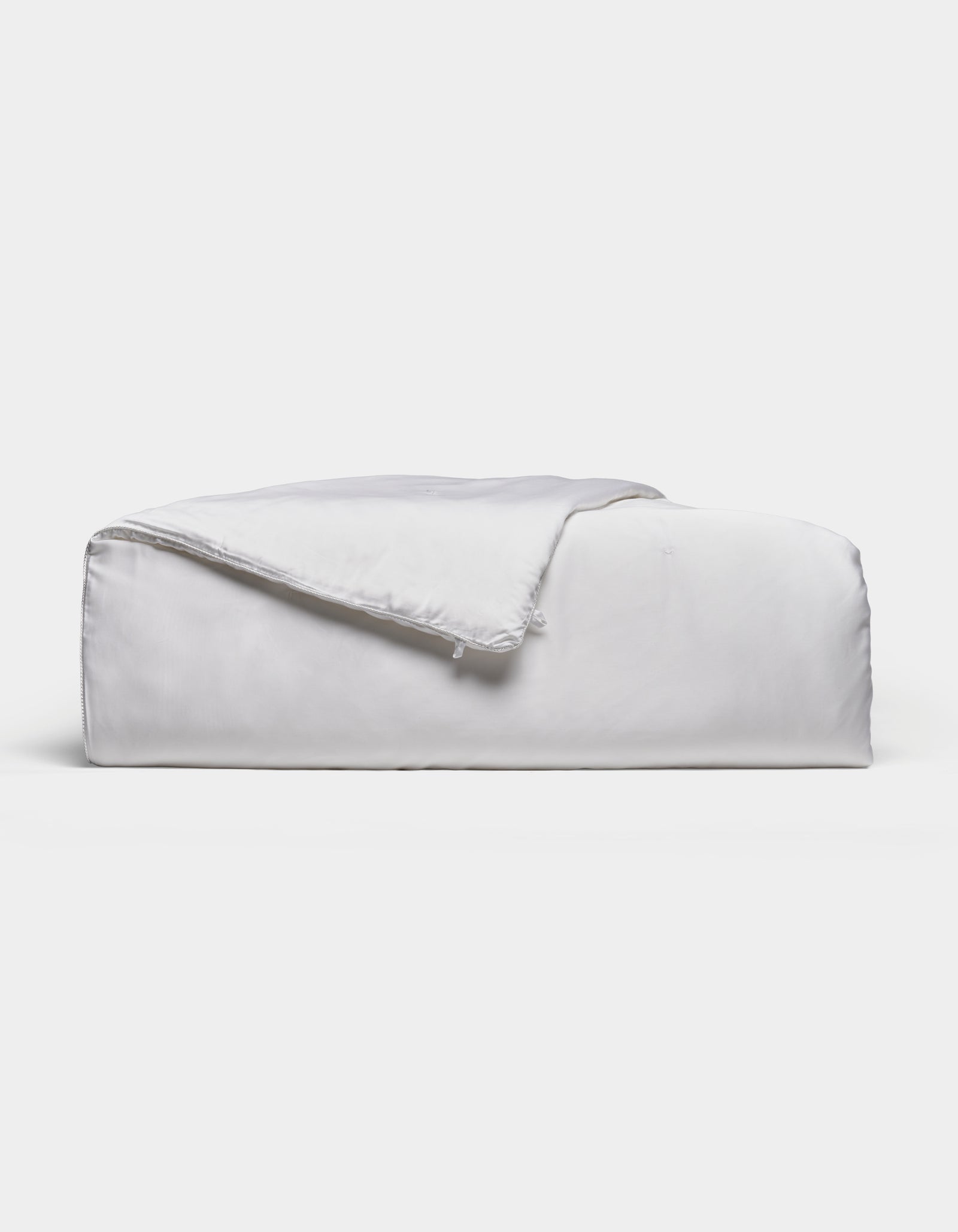 A neatly folded, fluffy Silk Comforter by Cozy Earth is placed against a plain light background. The fabric appears smooth and soft, highlighting its plush and inviting texture.