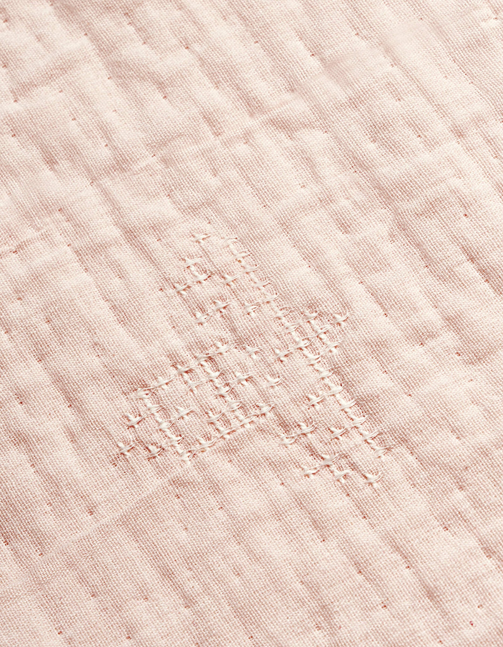 A close-up of the Cozy Earth Little Bee Matelasse Baby Blanket shows its white fabric with a grid-like, hand-stitched repair in matching thread, highlighting the textured and slightly uneven surface.