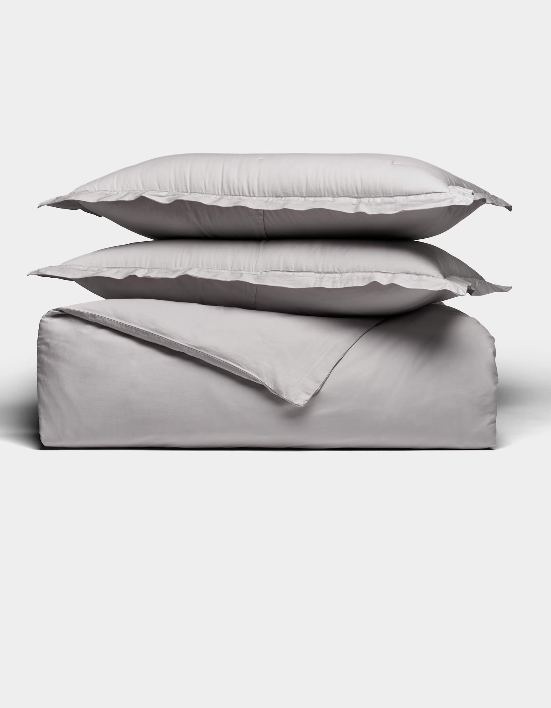 Two gray pillows rest atop a folded Soft-Wash Cotton Duvet Set by Cozy Earth, all neatly arranged against a plain white background.|Color:Dew