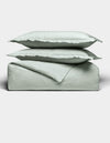 Two light gray pillows are stacked atop a matching folded Soft-Wash Cotton Duvet Set by Cozy Earth, all set against a plain white background. The bedding appears soft and smooth, highlighting its cozy and minimal aesthetic.|Color:Laurel