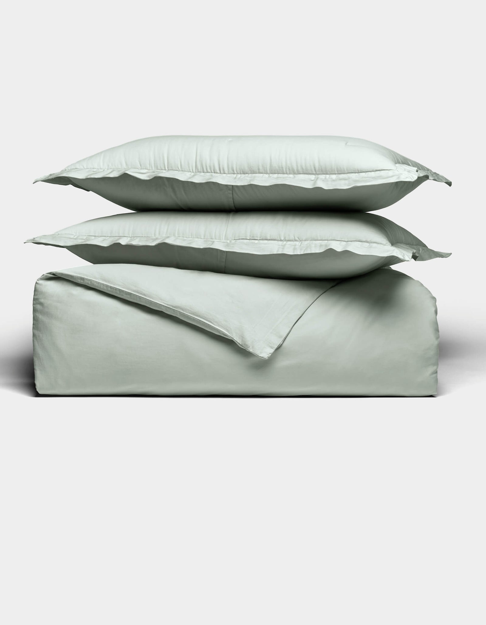 Two light gray pillows are stacked atop a matching folded Soft-Wash Cotton Duvet Set by Cozy Earth, all set against a plain white background. The bedding appears soft and smooth, highlighting its cozy and minimal aesthetic.