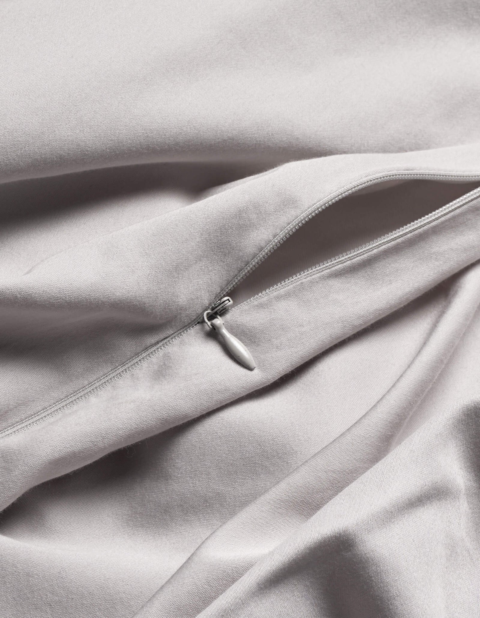 A close-up of Cozy Earth's Soft-Wash Cotton Duvet Cover in light grey shows a silver zipper partially unzipped on its smooth, gently folded fabric.