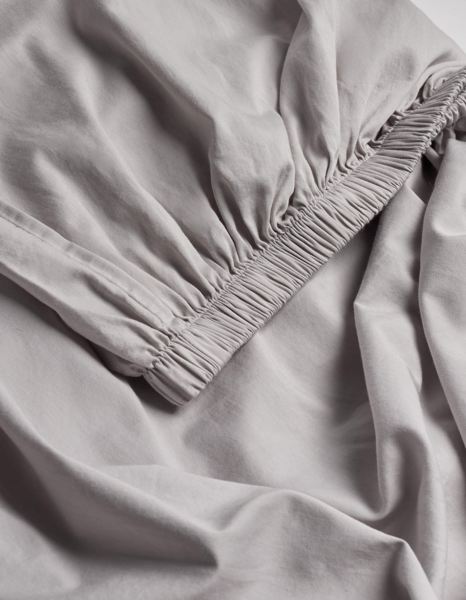 A close-up of the Cozy Earth Soft-Wash Cotton Fitted Sheet highlights its light gray color, gathered elastic edge, and ultra-soft fabric texture.