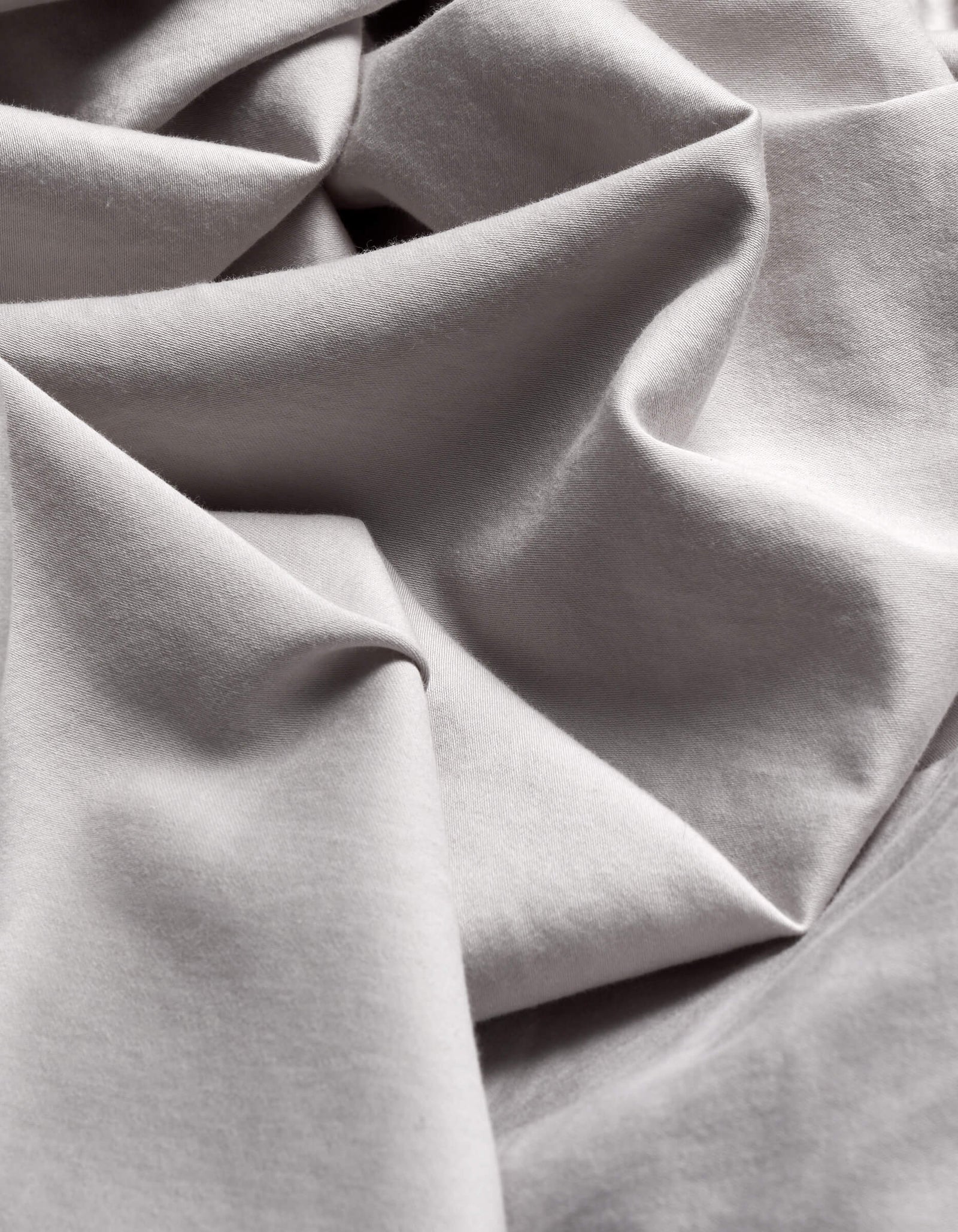 Close-up of the Cozy Earth Soft-Wash Cotton Flat Sheet in light grey, featuring flowing folds and gentle shadows that highlight its smooth texture and elegant drape.