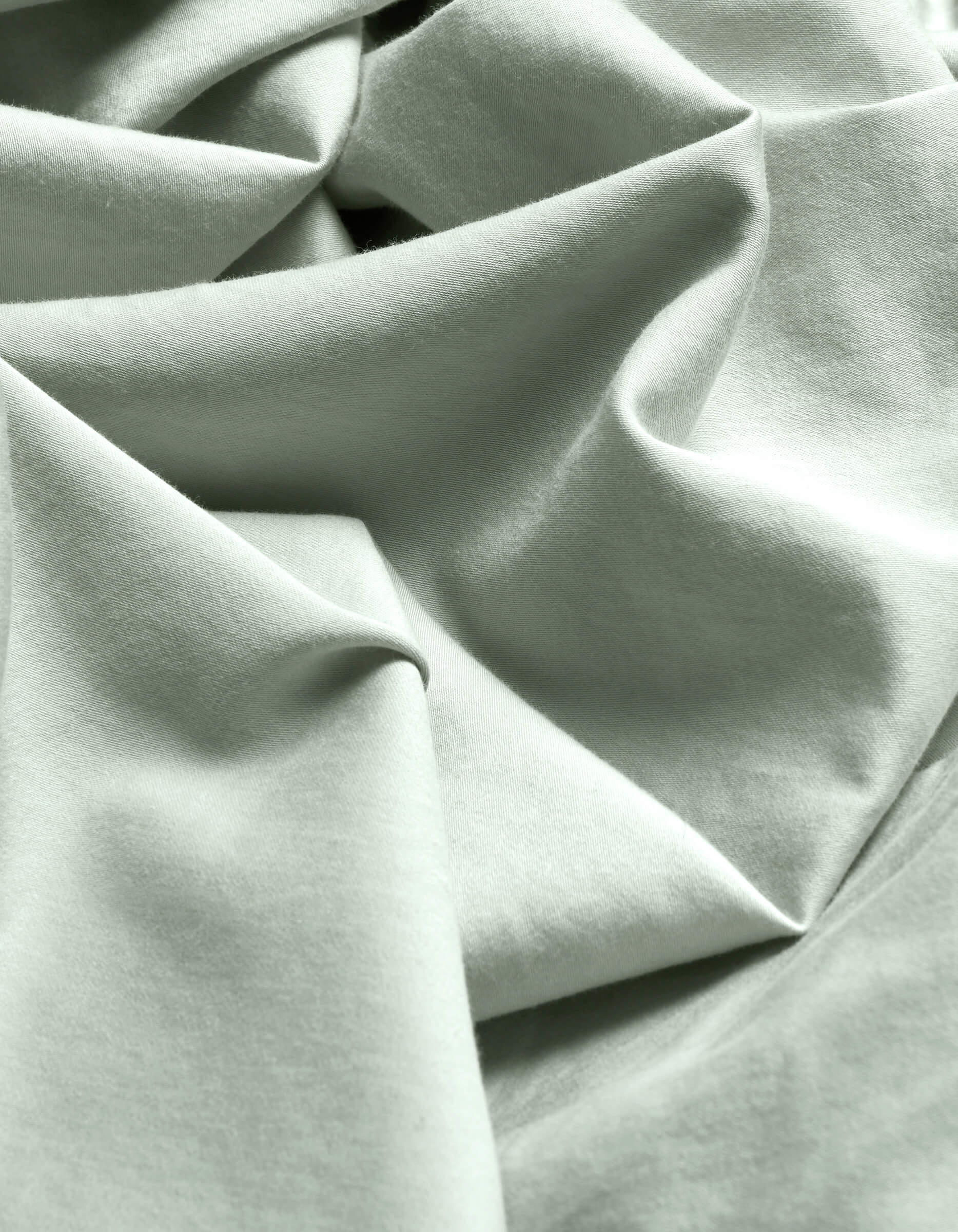 Close-up of Cozy Earth's Soft-Wash Cotton Flat Sheet in light mint green, featuring soft folds, gentle wrinkles, a subtle weave, and delicate shadows.|Color:Laurel