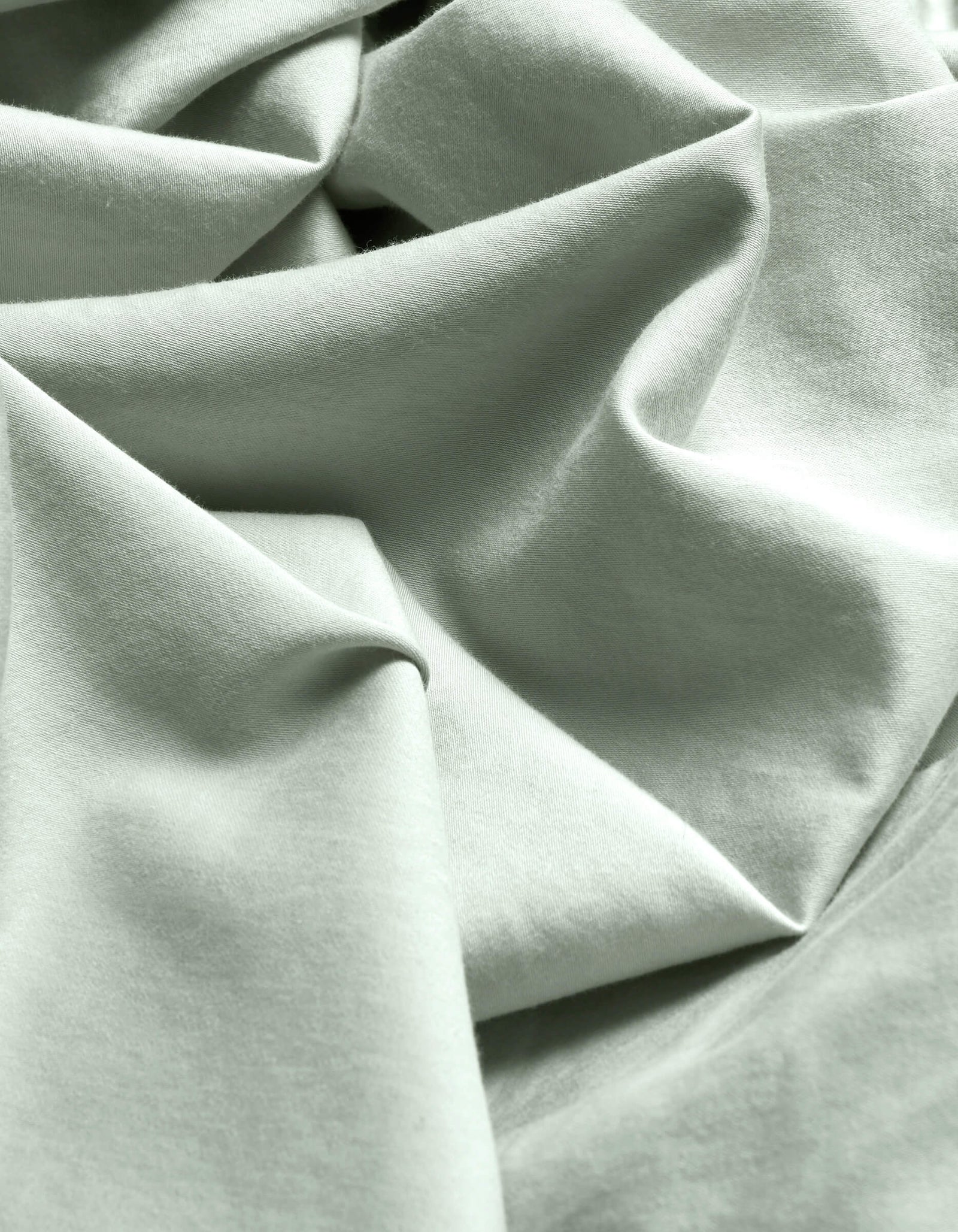 Close-up of Cozy Earth's Soft-Wash Cotton Flat Sheet in light mint green, featuring soft folds, gentle wrinkles, a subtle weave, and delicate shadows.