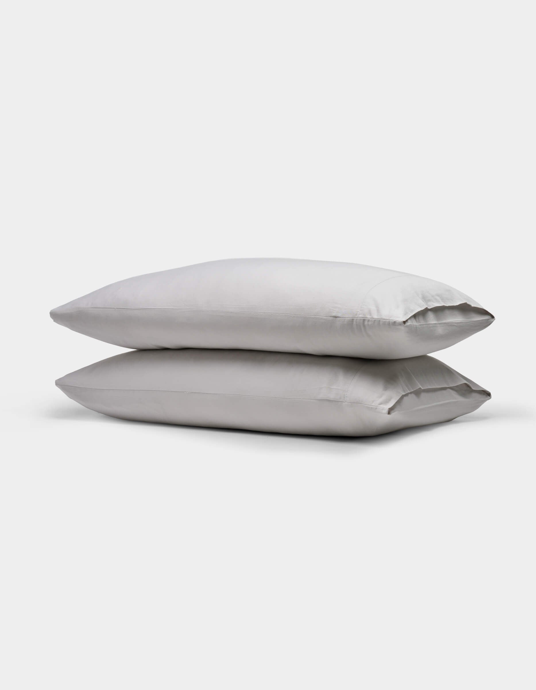 Two stacked, rectangular Soft-Wash Cotton Pillowcases by Cozy Earth in light gray are shown on a plain white background.|Color:Dew
