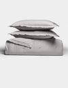 Two light gray pillows rest atop a folded Soft-Wash Cotton Quilt Set by Cozy Earth, arranged neatly against a plain white background. The bedding looks exceptionally soft and inviting.|Color:Dew