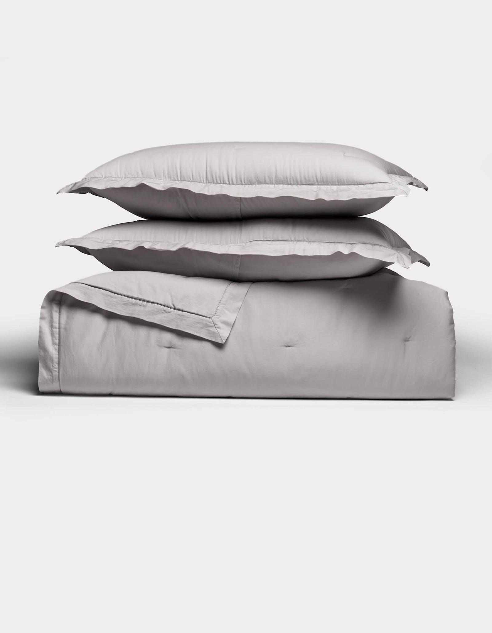 Two light gray pillows rest atop a folded Soft-Wash Cotton Quilt Set by Cozy Earth, arranged neatly against a plain white background. The bedding looks exceptionally soft and inviting.