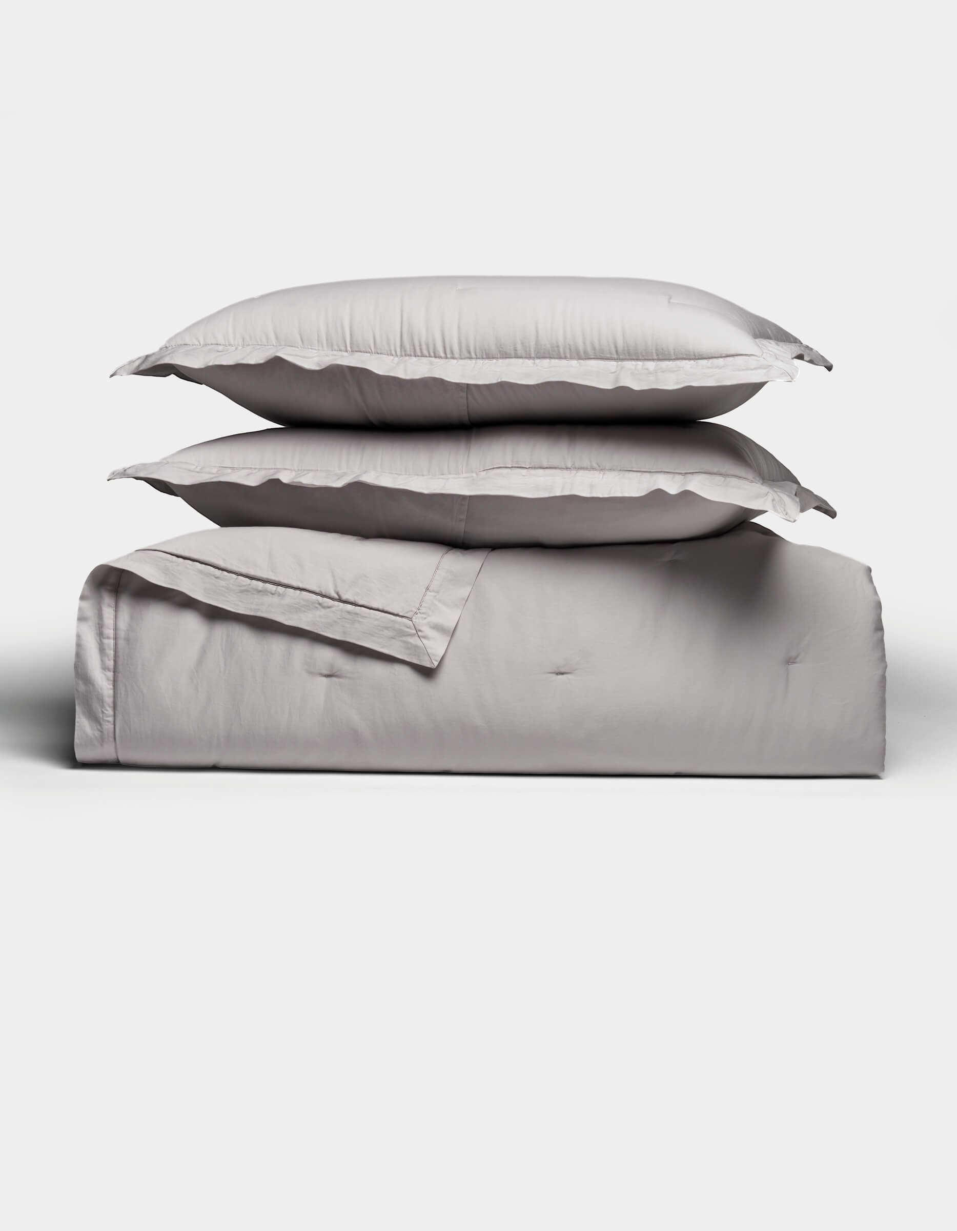 Two light gray pillows rest atop a folded Soft-Wash Cotton Quilt Set by Cozy Earth, arranged neatly against a plain white background. The bedding looks exceptionally soft and inviting.|Color:Dew