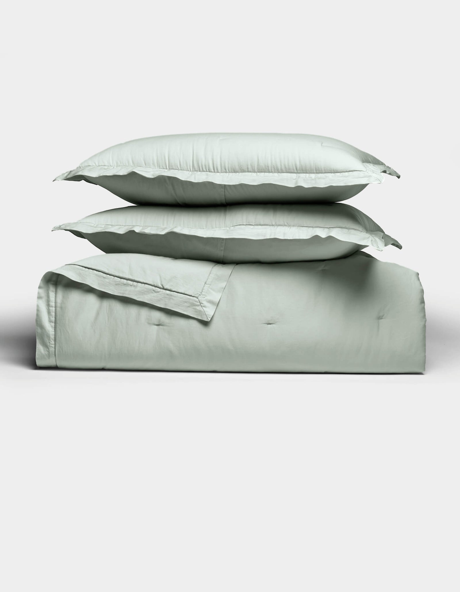 The Cozy Earth Soft-Wash Cotton Quilt Set, neatly folded in light green with matching pillowcases stacked on top, is displayed against a plain white background.